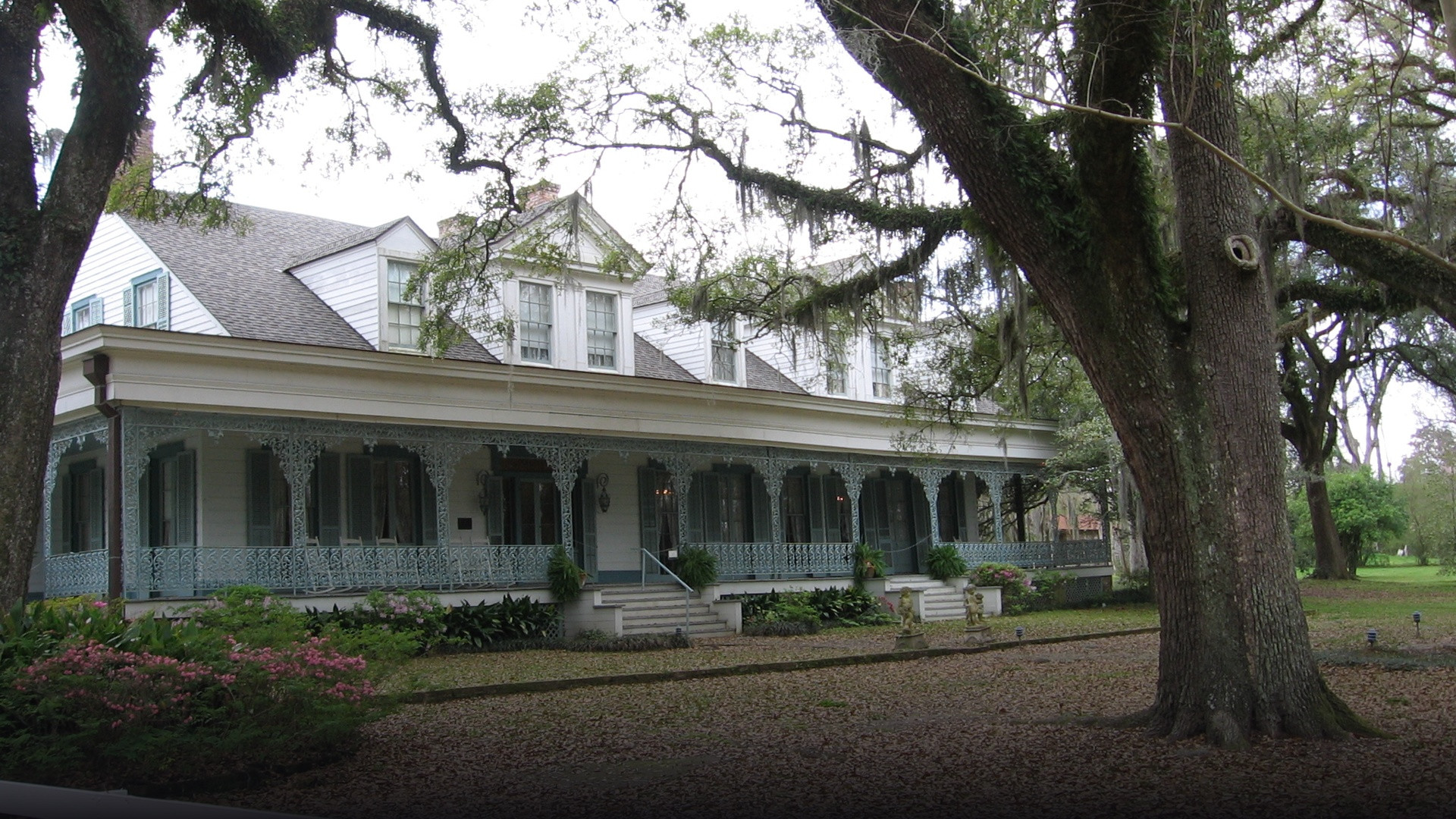 Sprawling antebellum porch and historic facade of The Myrtles Plantation shaded by mature oak trees in Louisiana.