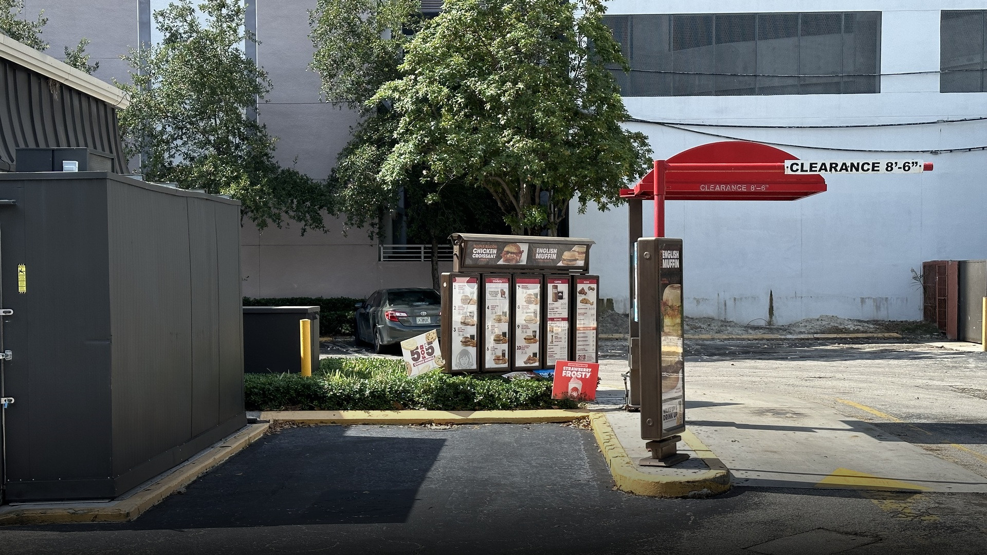 A fast-food drive-thru ordering lane with menu board, speaker post, and vehicle clearance barrier.