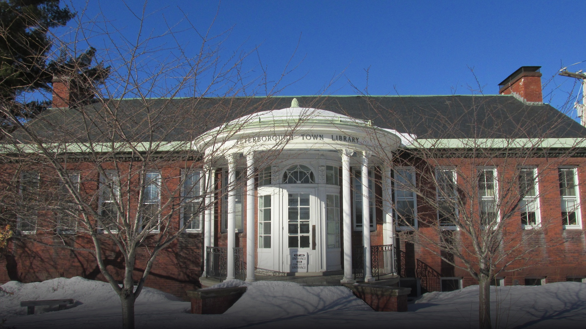 Exterior view of the historic red brick Peterborough Town Library surrounded by lush green trees.