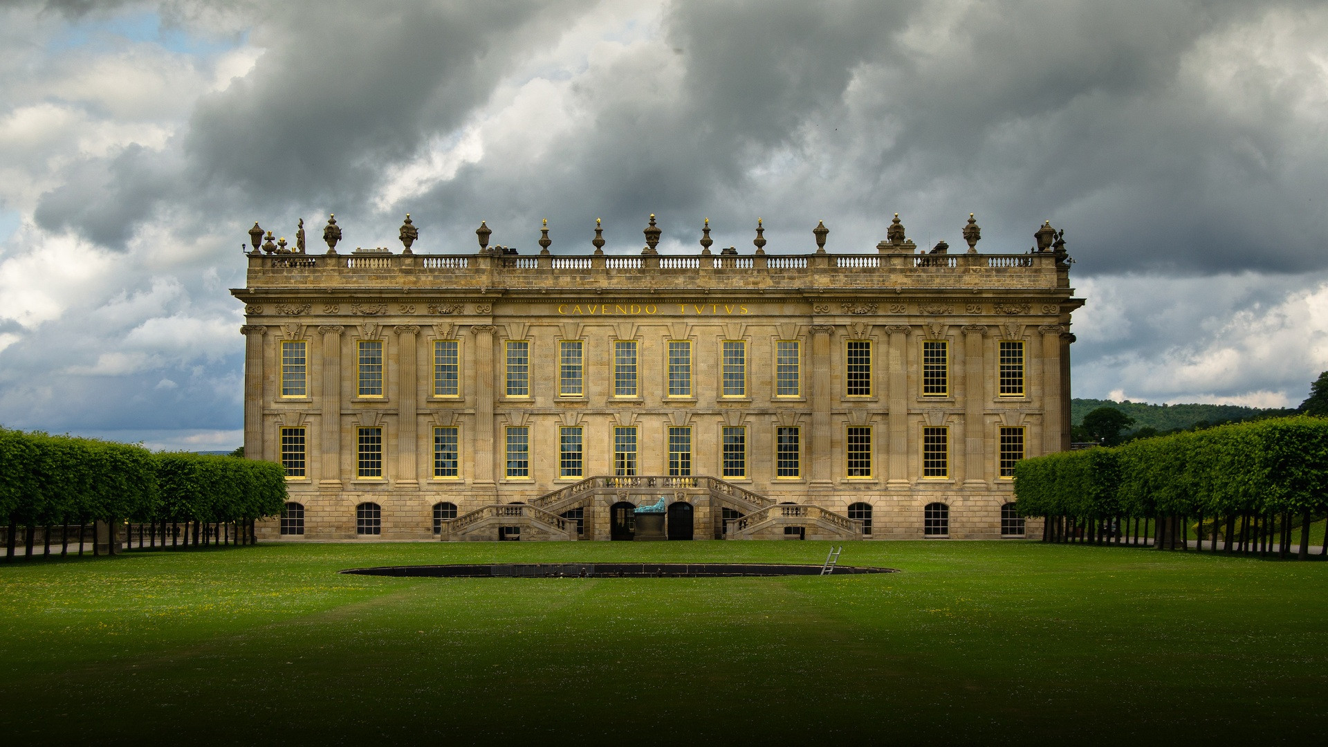 The grand English Baroque south facade of Chatsworth House standing before a broad emerald lawn under moody skies.