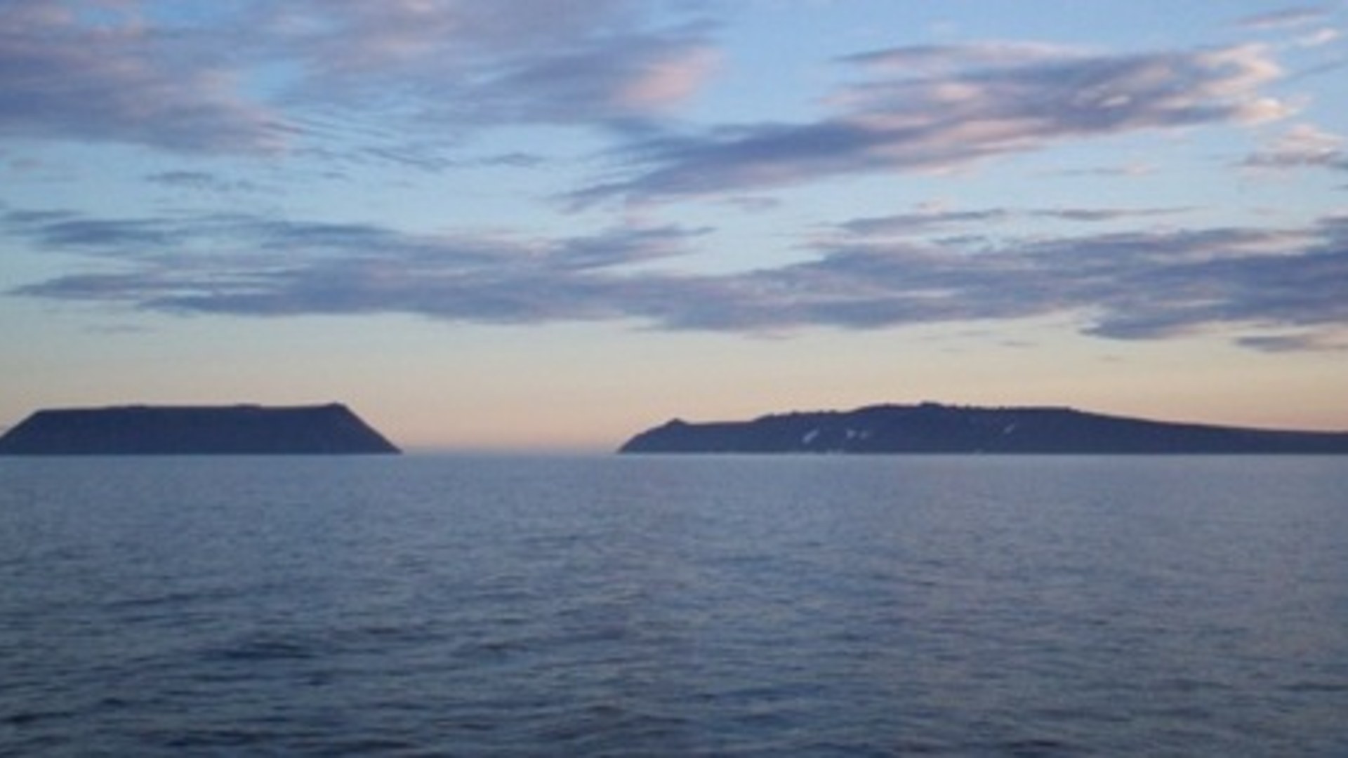 Wide landscape photograph of Little Diomede Island and Big Diomede Island facing each other across the Bering Sea between the US and Russia.