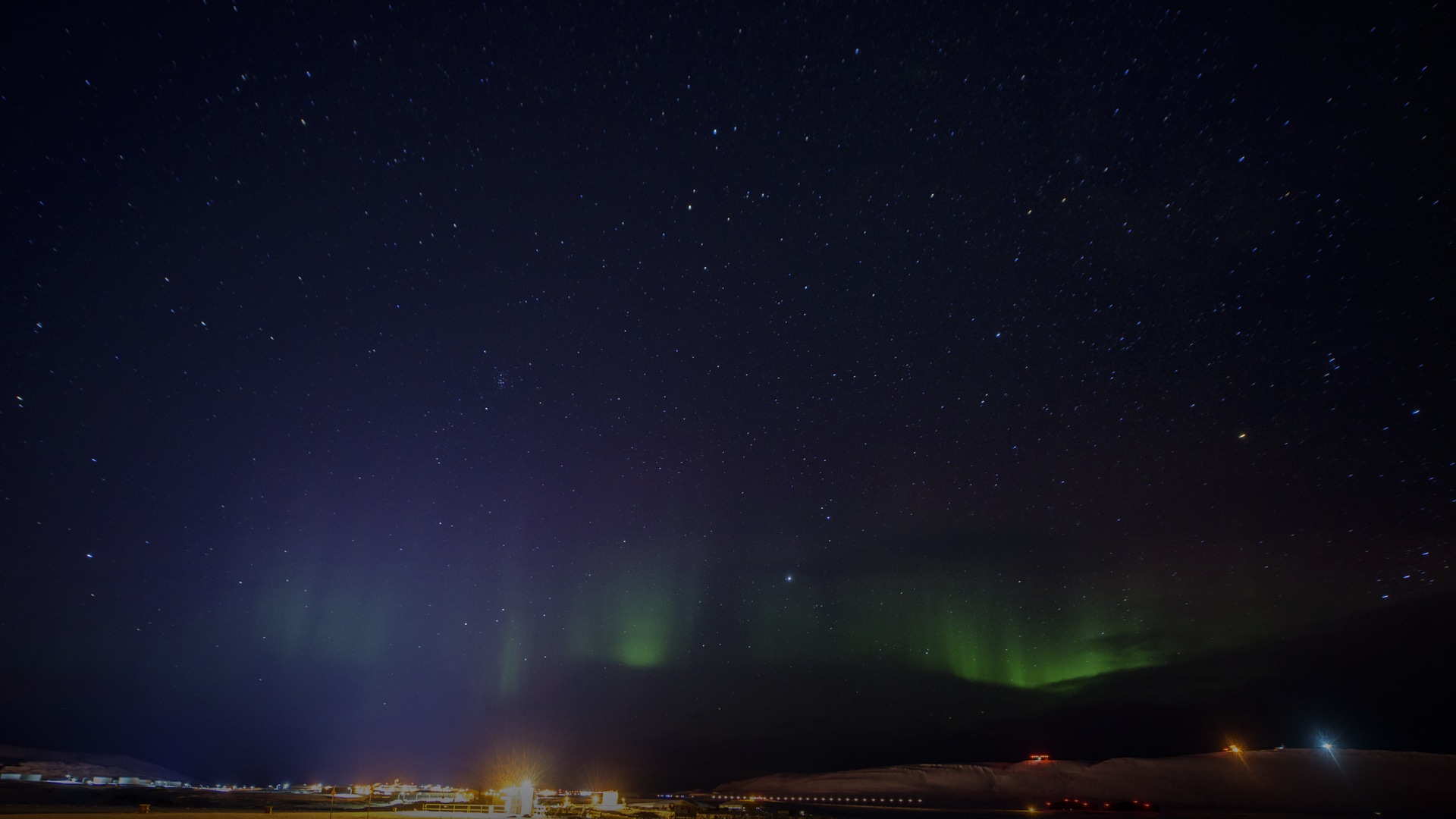 Luminous emerald green Aurora Borealis curtain shimmering across the star-filled Arctic night sky over Greenland.