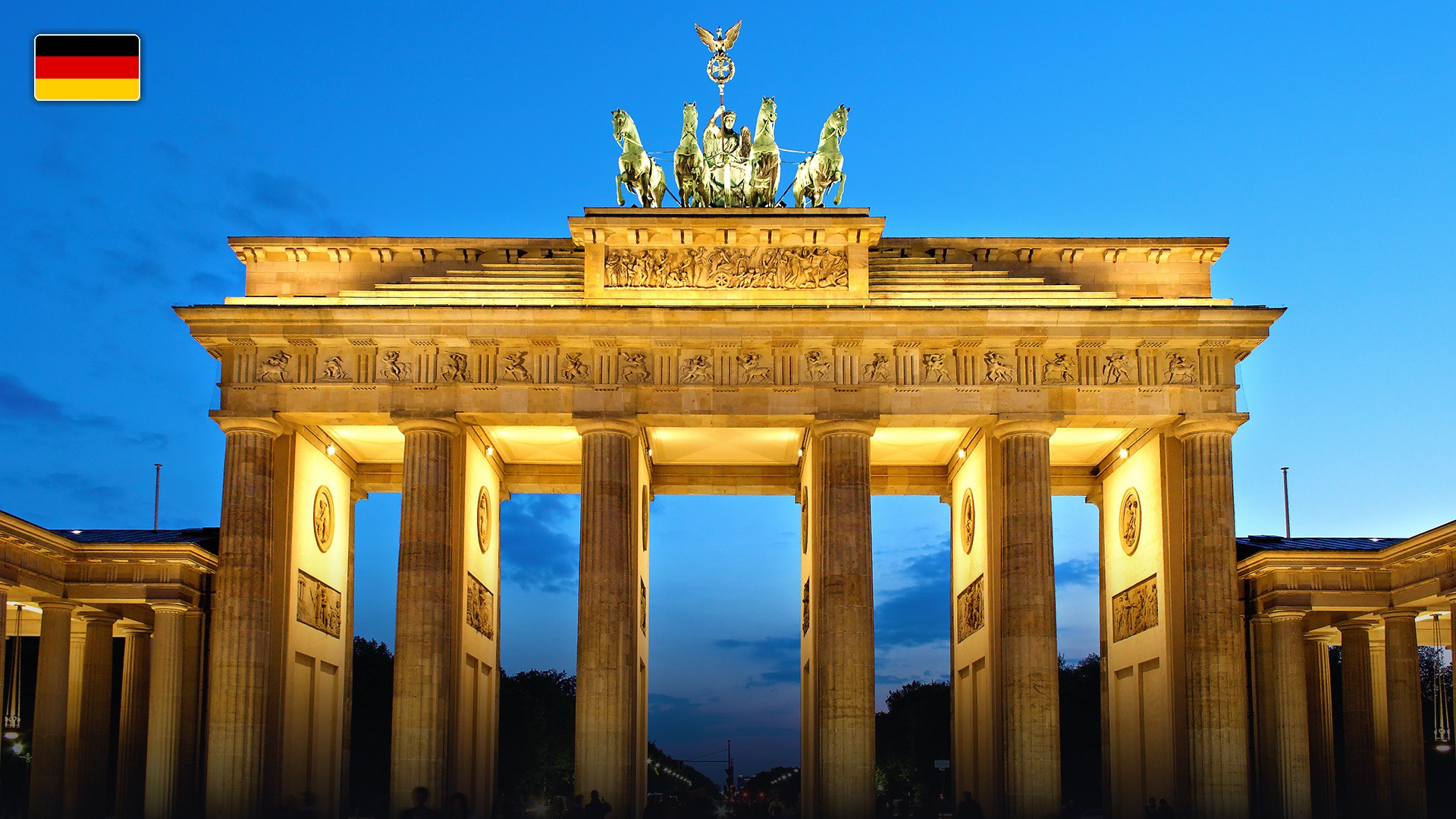 The neoclassical Brandenburg Gate illuminated in Berlin, with the flag of Germany.