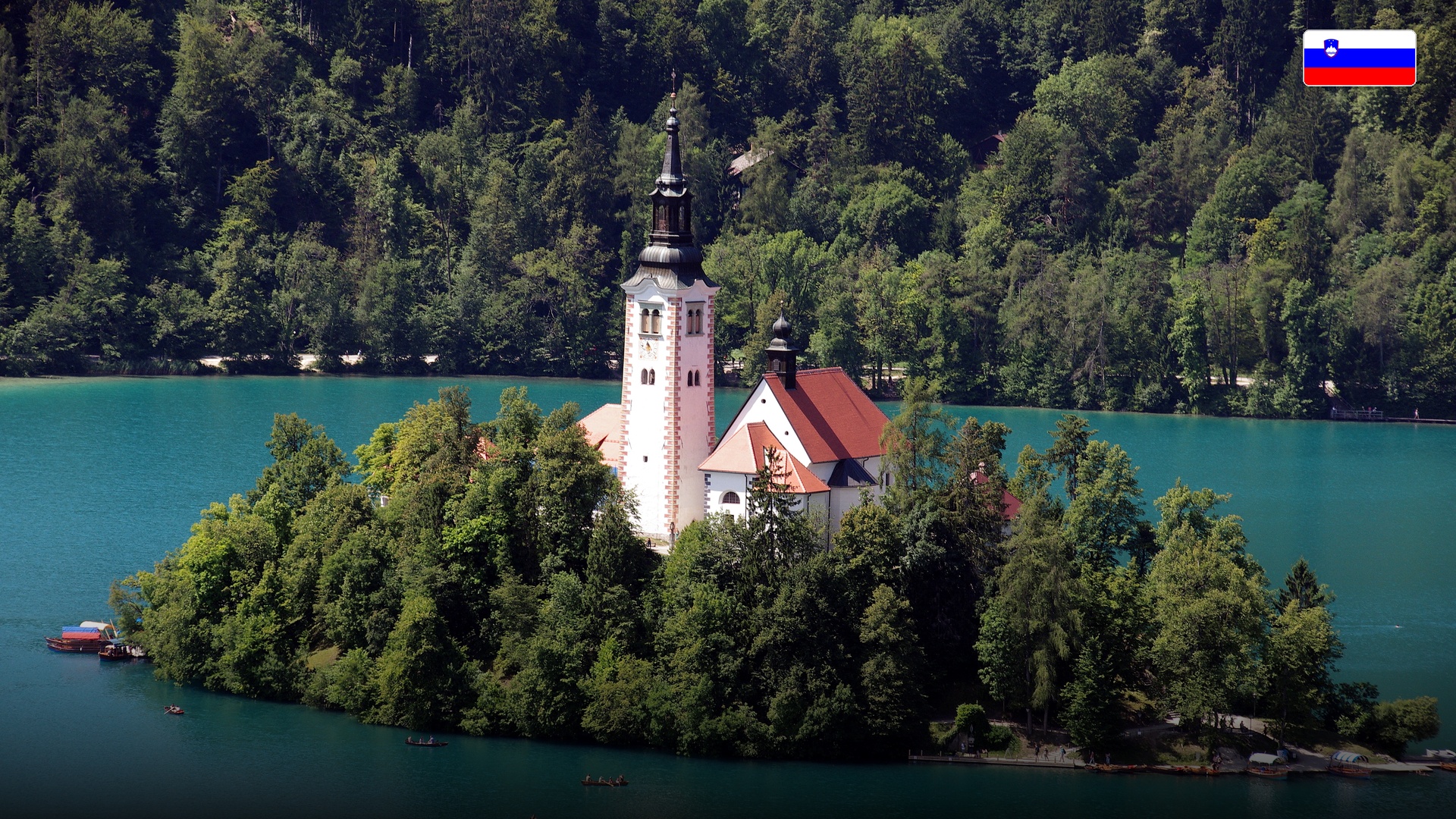 Scenic close-up of the pilgrimage church on Lake Bled island with its bell tower surrounded by turquoise waters.
