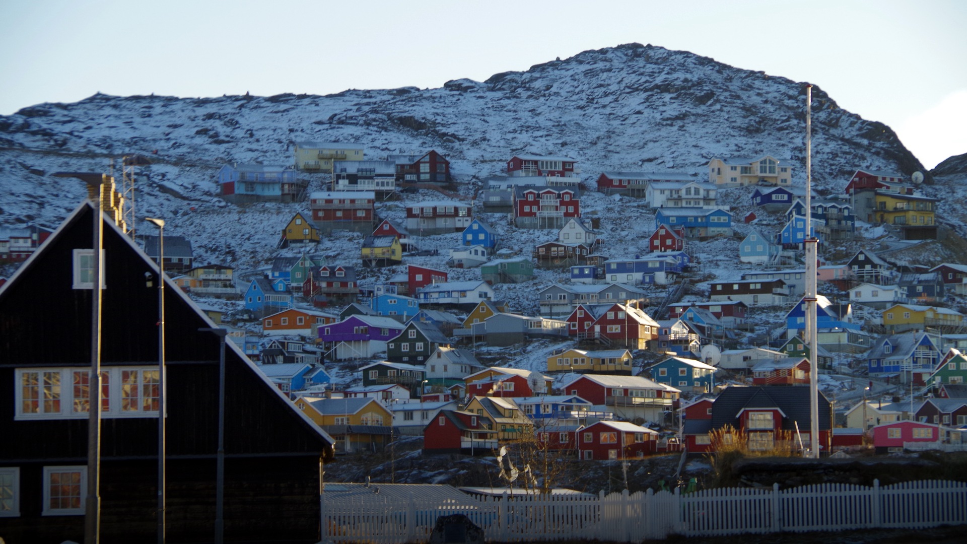 Vivid yellow, red, and blue wooden houses perched across rocky coastal hills overlooking the harbor in Qaqortoq.