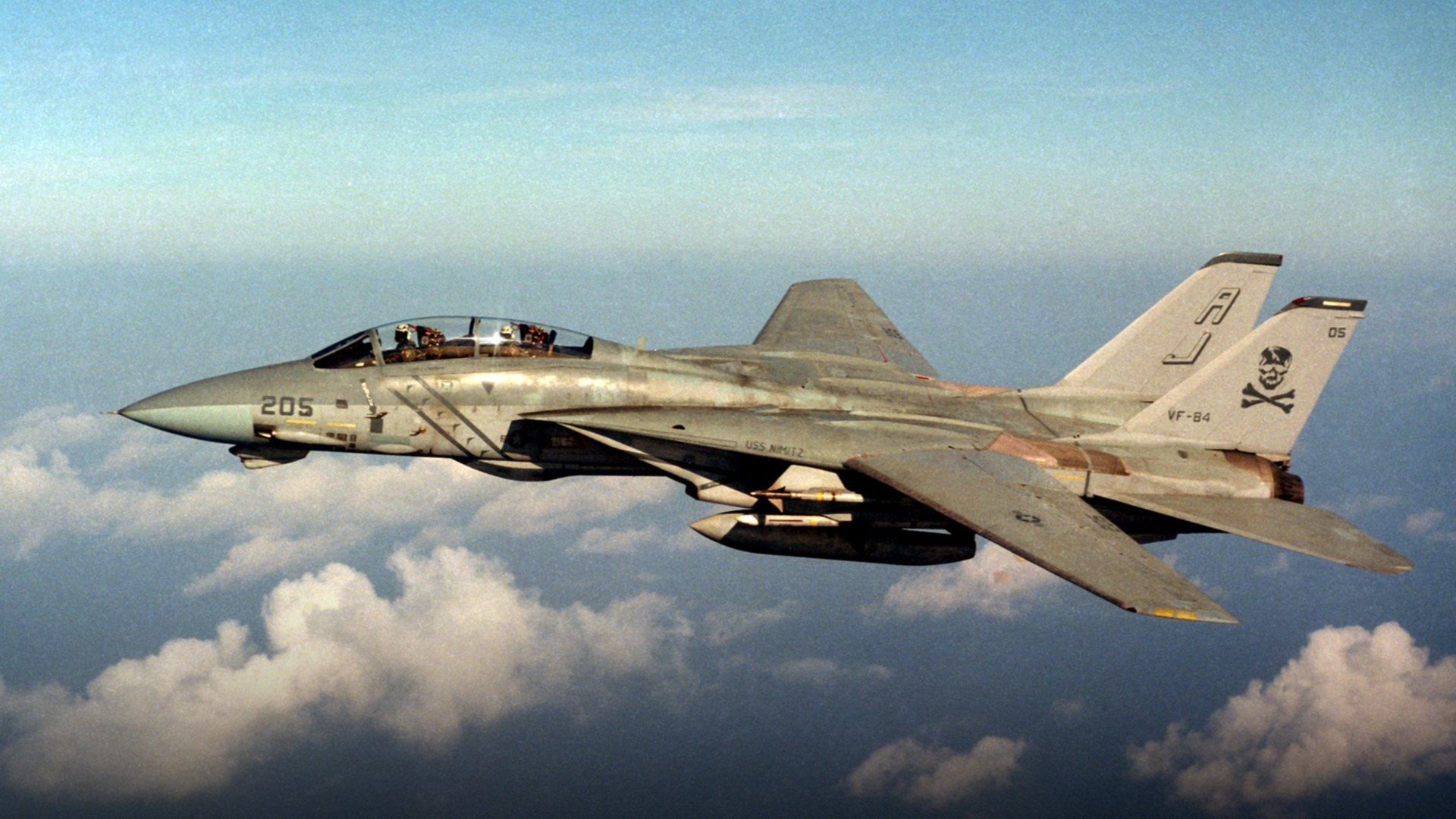 Grumman F-14A Tomcat of VF-84 Jolly Rogers in flight with iconic black tail and skull insignia.