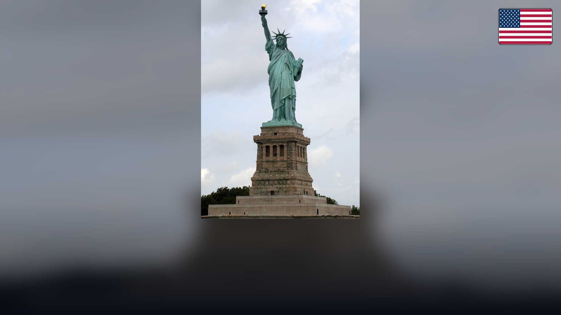 Statue of Liberty overlooking New York Harbor with the American flag in the top right corner.