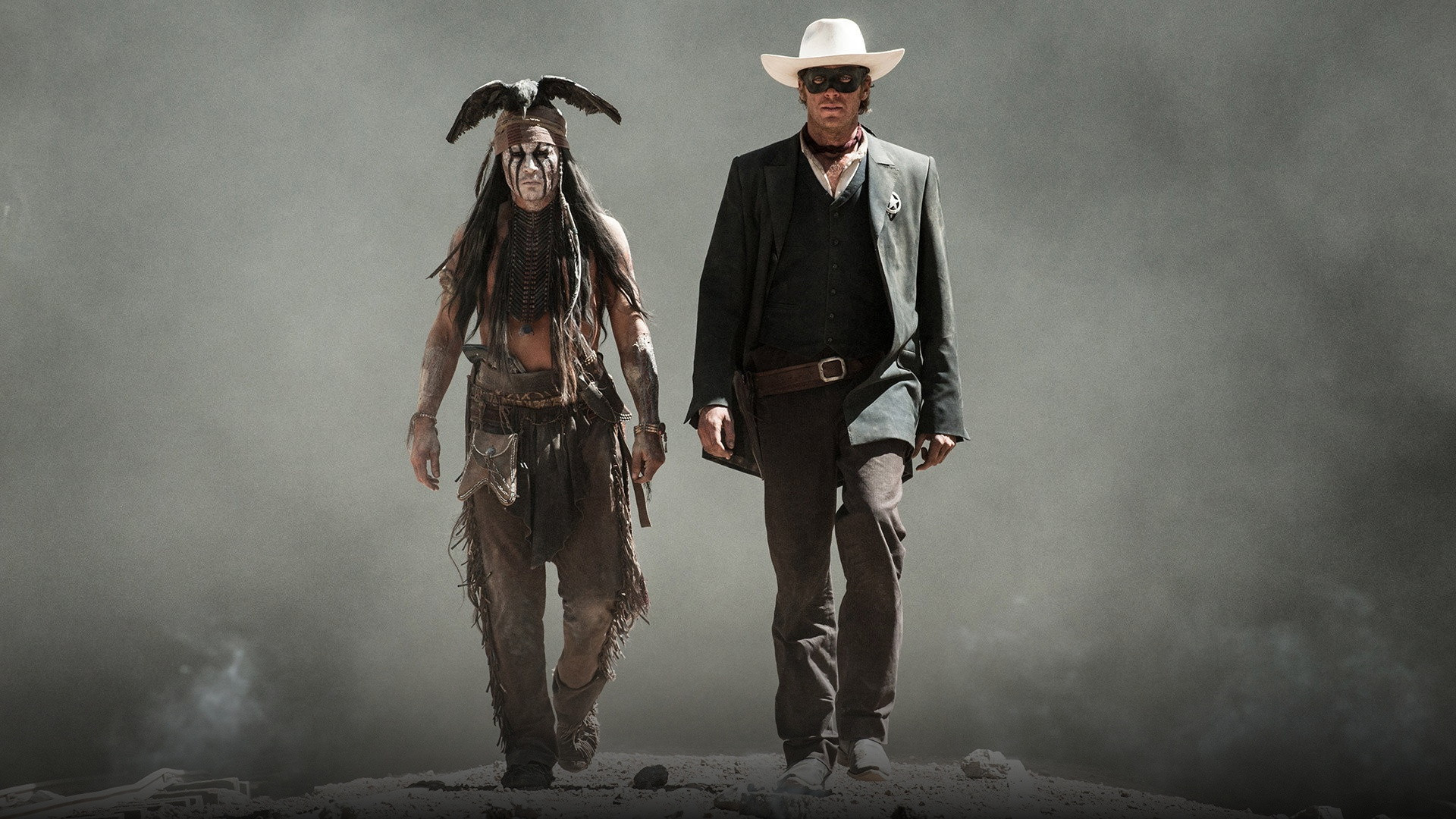 The Lone Ranger and Tonto striding forward through dust and smoke across a desert plain.