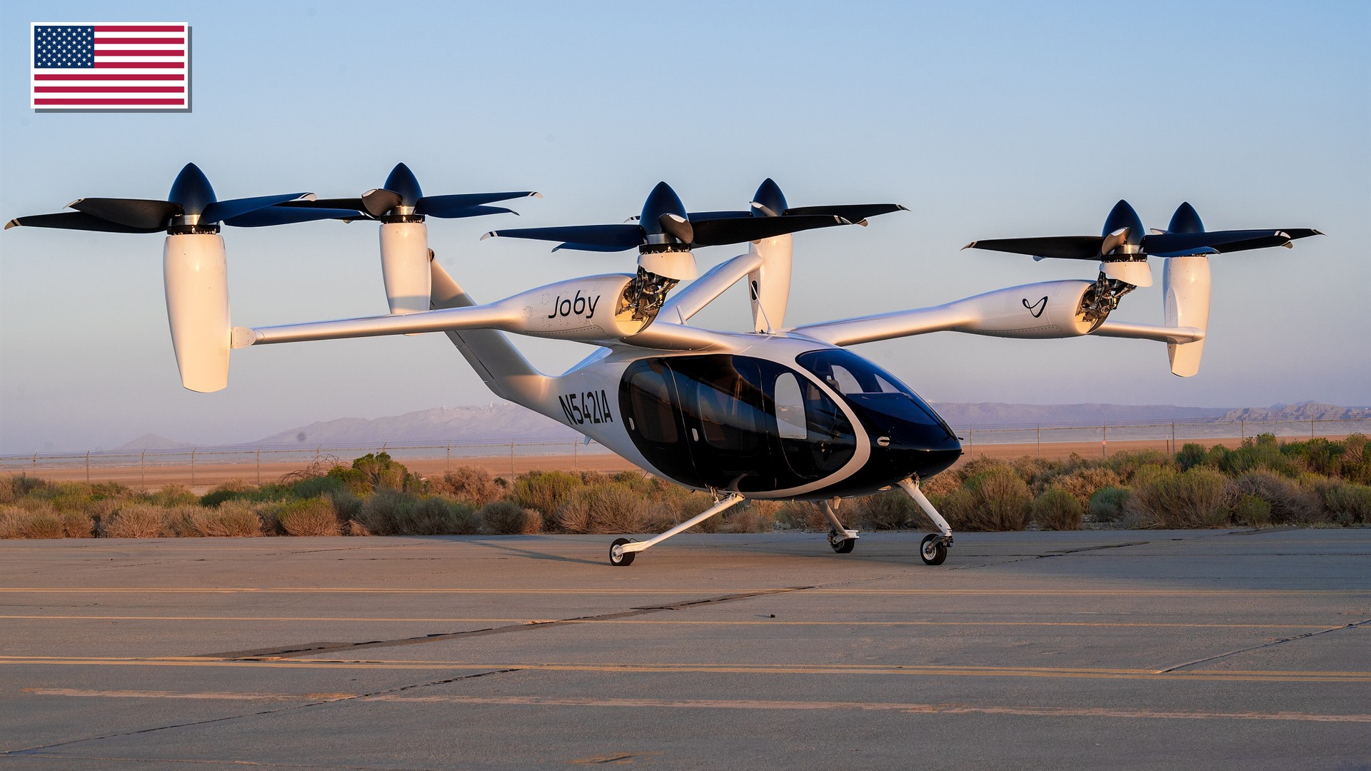 Joby Aviation S4 experimental eVTOL tilt-rotor aircraft at Edwards Air Force Base with the US flag in the top-left corner.
