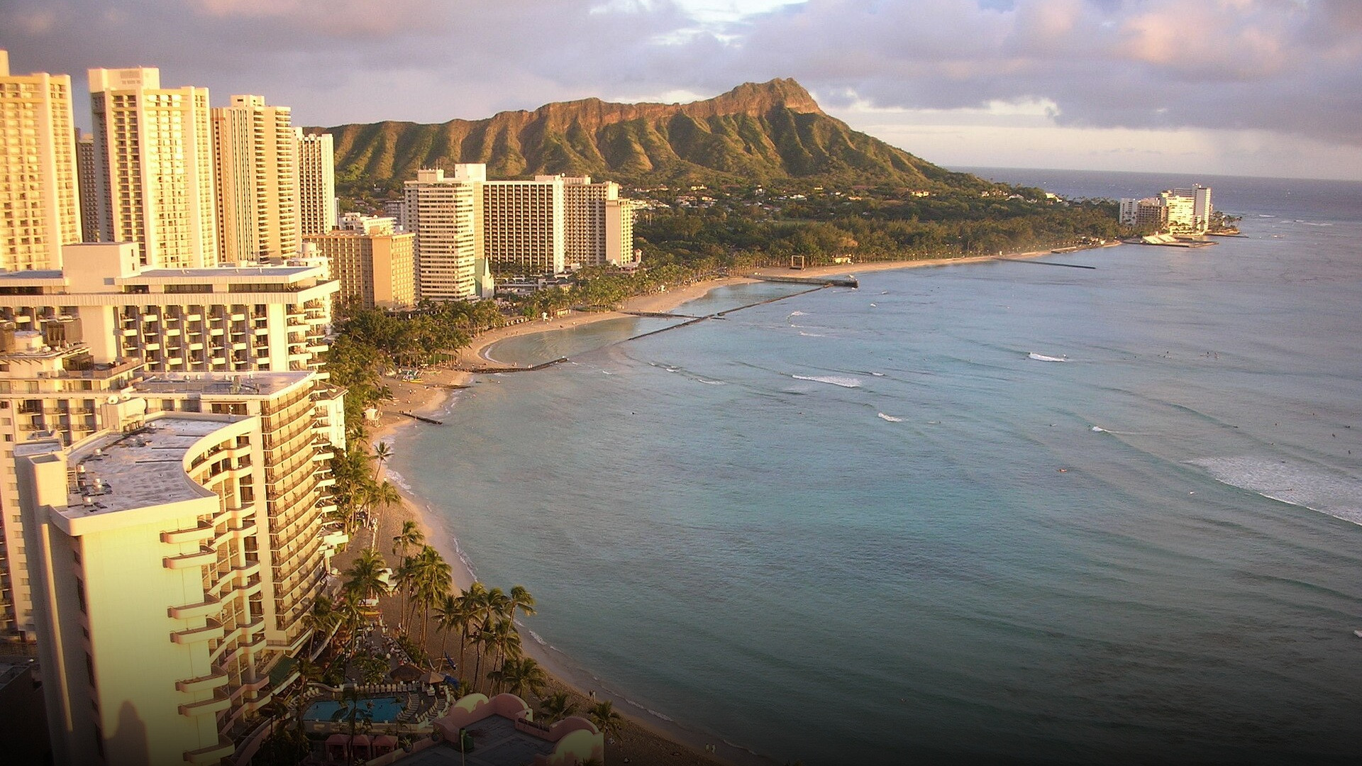 Vibrant sunset framing palm trees and gentle waves along the shores of Waikiki Beach.