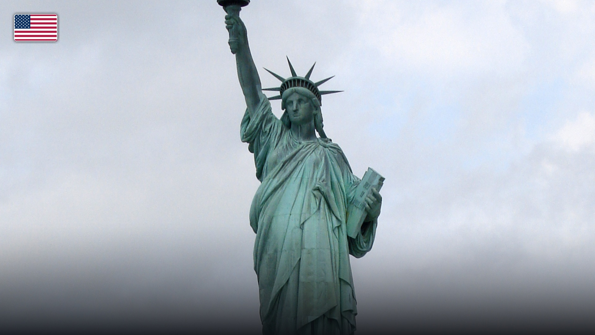 The Statue of Liberty standing tall in New York Harbor, with the flag of the United States.