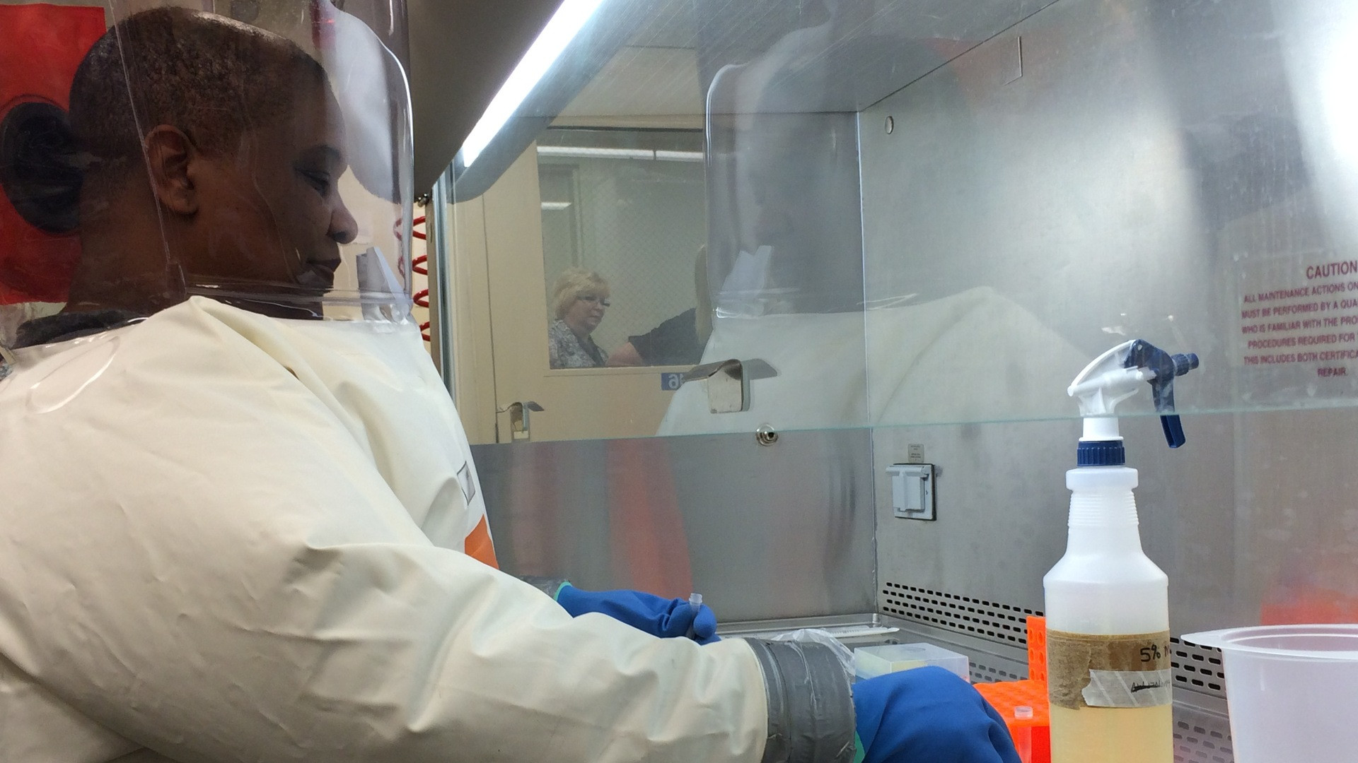 Scientist in a pressurized BSL-4 protective biocontainment suit working inside an airtight isolation laboratory.