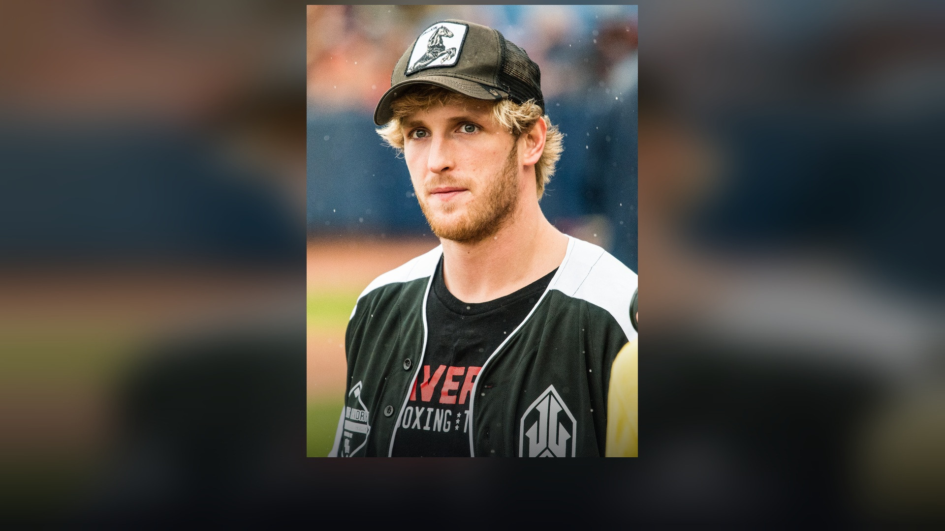 Logan Paul wearing a cap and sports jersey at an athletic event.