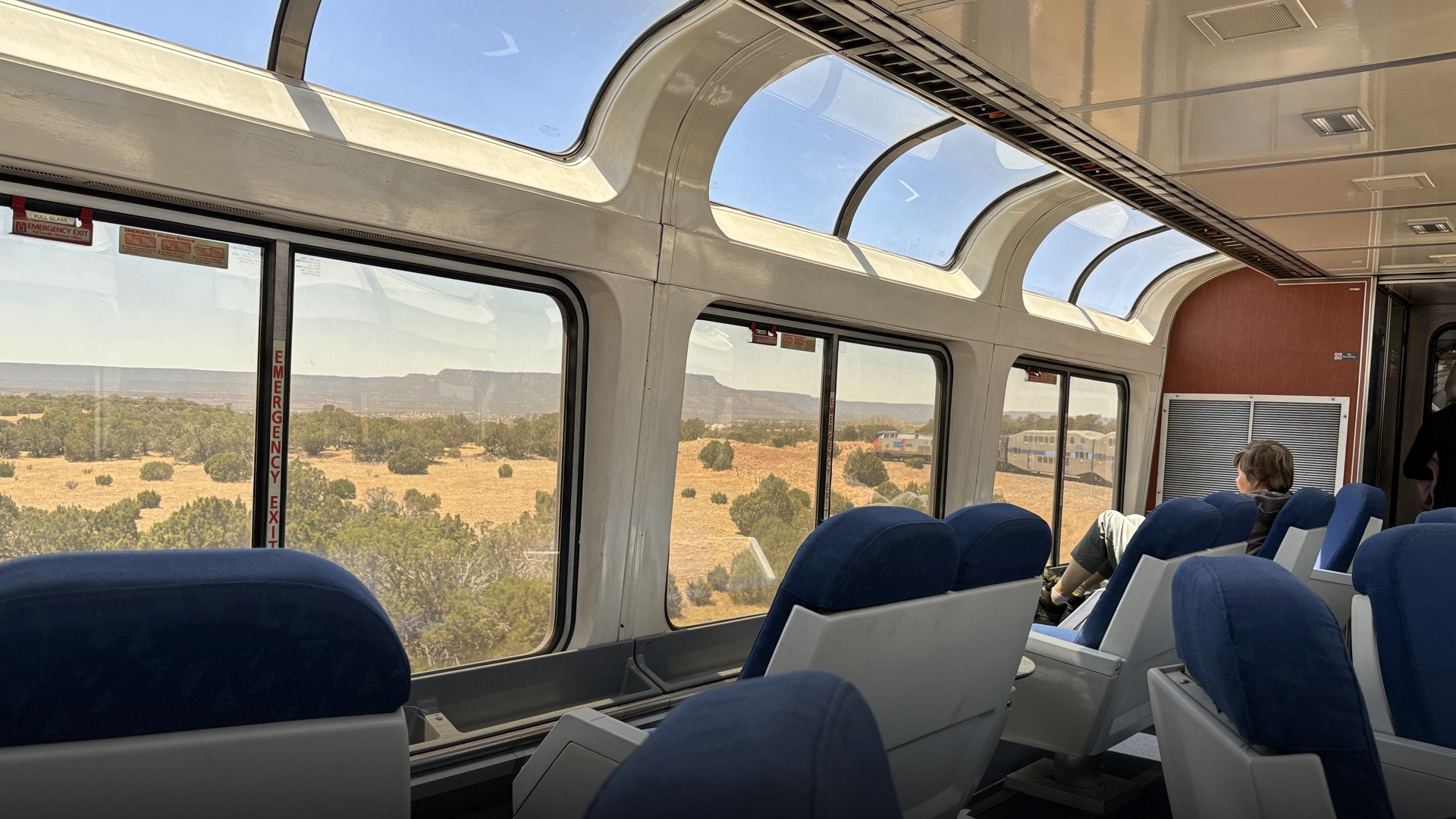 Interior view of an Amtrak Sightseer Lounge car with panoramic wrap-around windows looking out onto New Mexico desert mesas