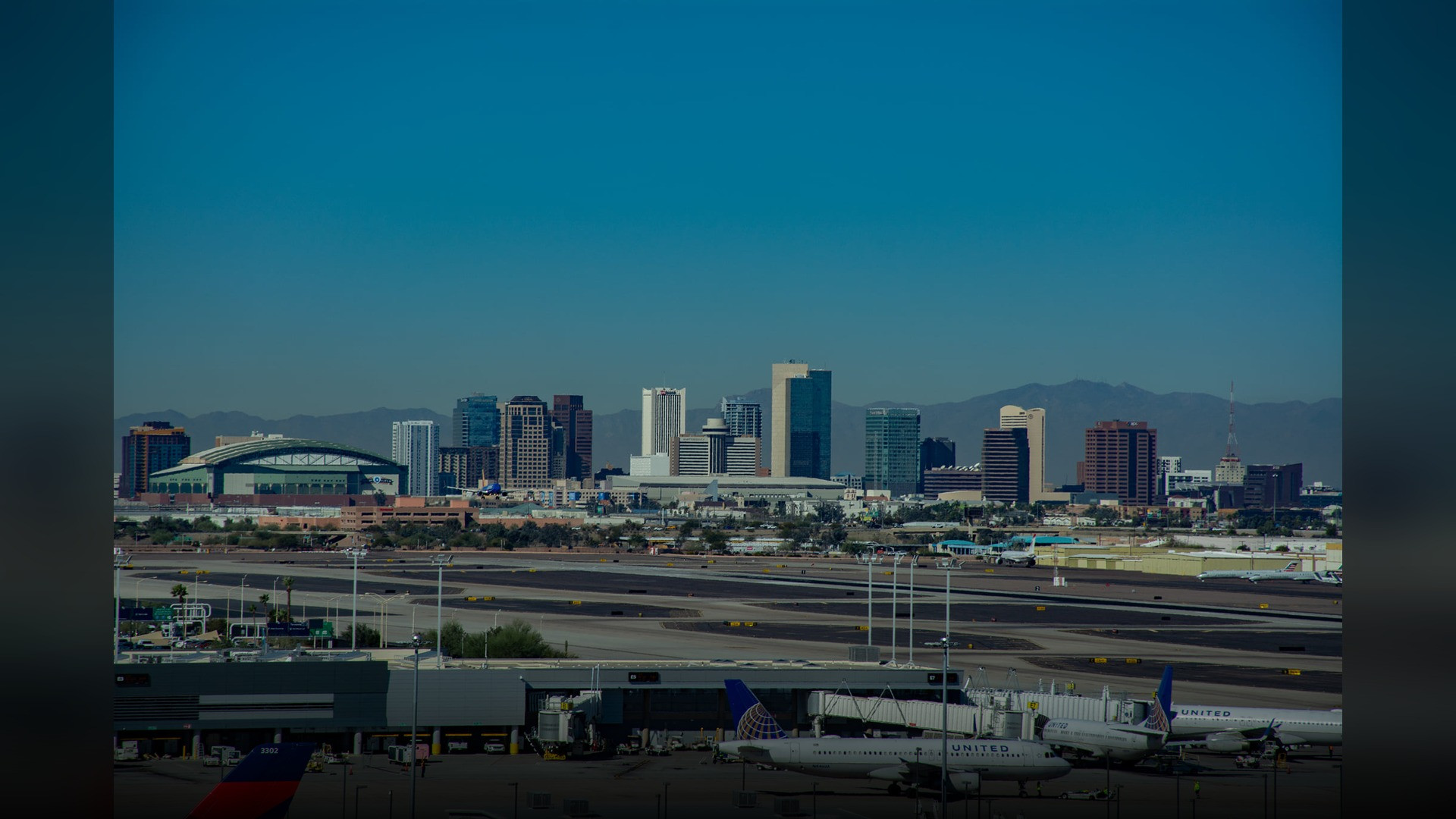 An elevated view of Phoenix Sky Harbor International Airport with the PHX Sky Train and desert mountains in background.