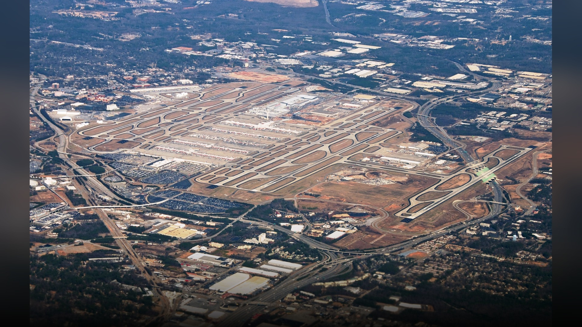 An aerial view of the massive terminal complex, parallel runways, and parked jetliners at Hartsfield-Jackson Atlanta International Airport.