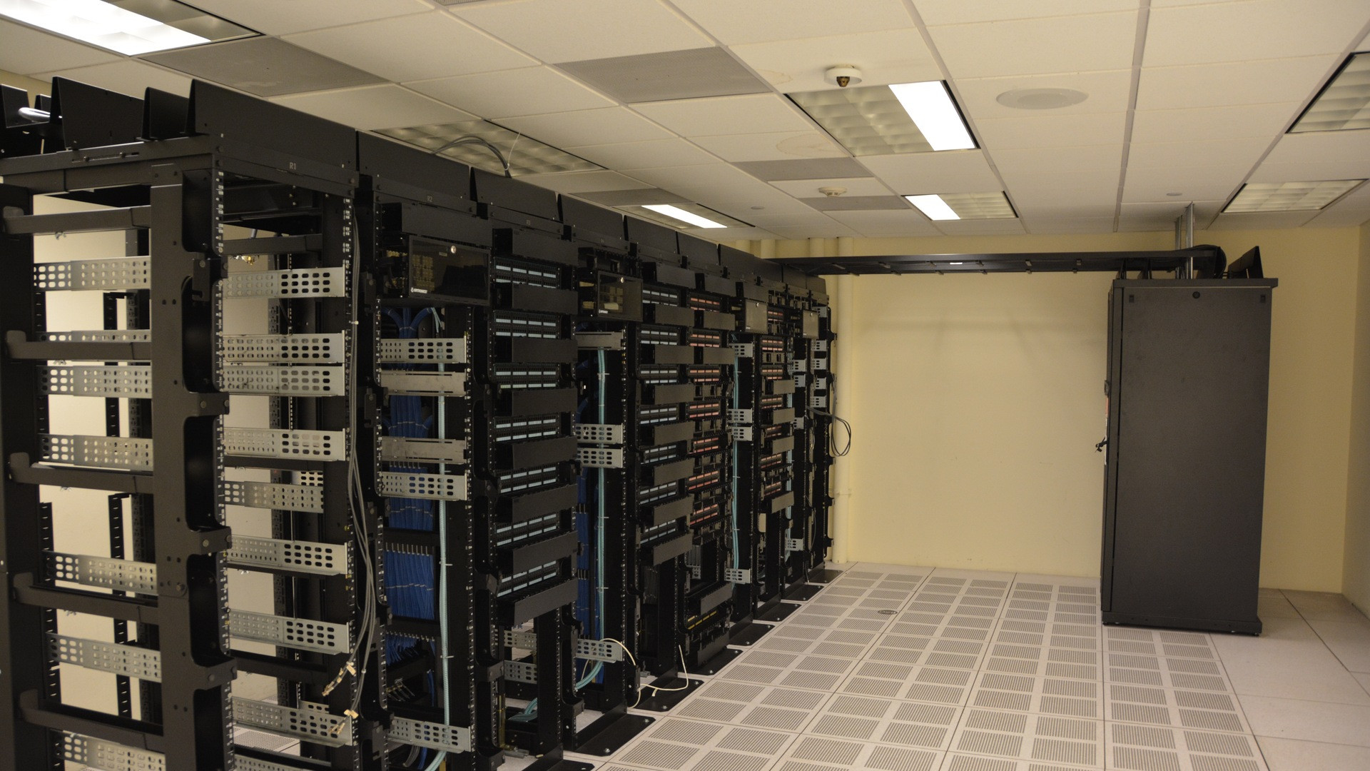 Perspective shot down a long, blue-lit data center corridor lined with server racks stretching into darkness.