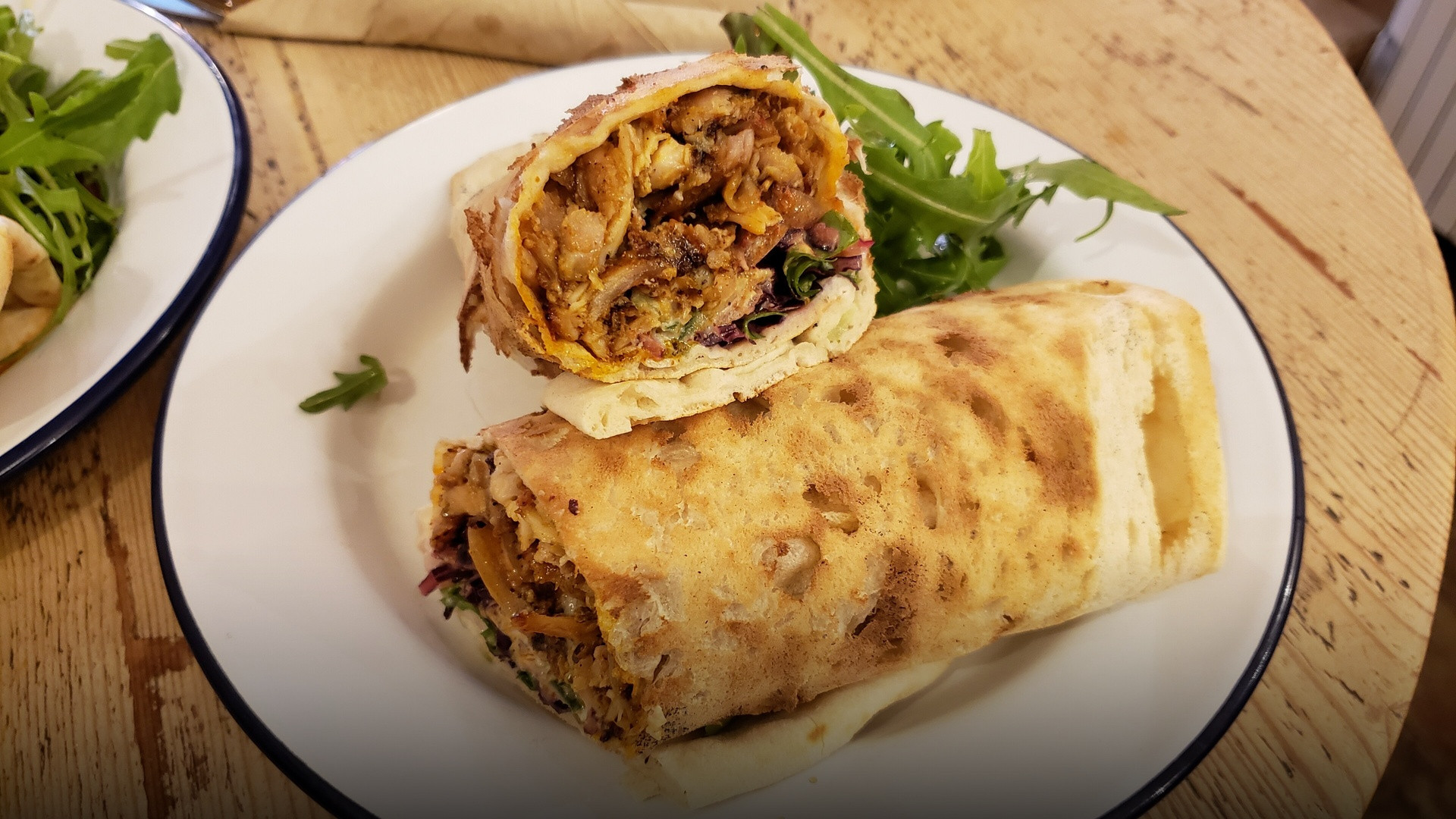 A freshly rolled and toasted chicken shawarma wrap cut open to show seasoned shaved meat, garlic sauce, and pickles.