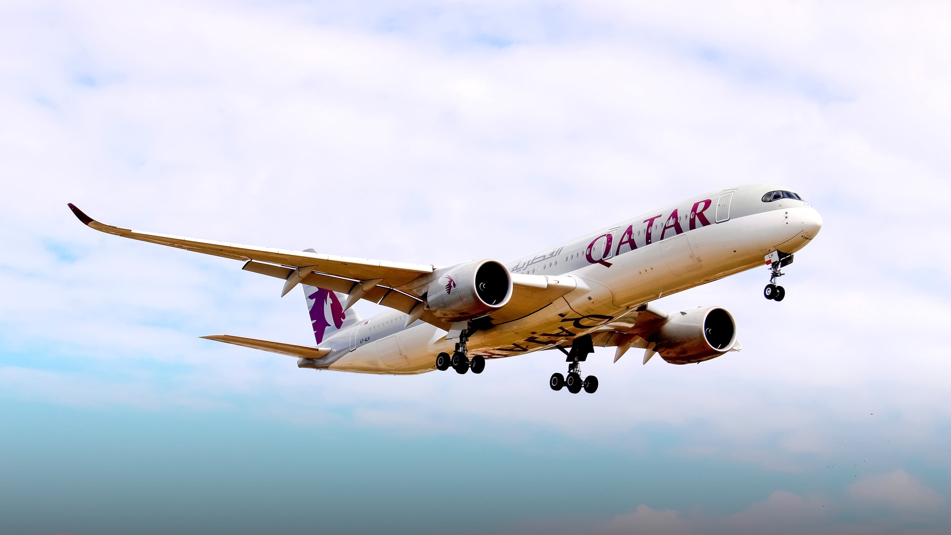 A pristine Qatar Airways Airbus A350-941 flagship jetliner cruising smoothly through calm blue skies.