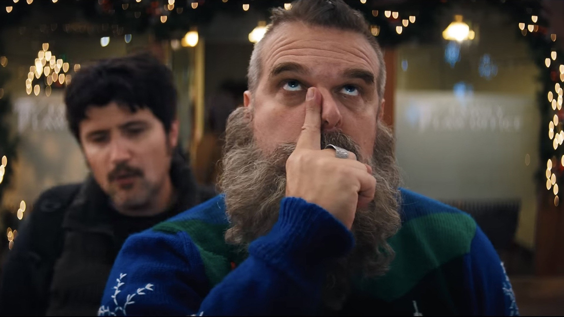 David Harbour as a rugged, bearded Santa Claus in a festive holiday sweater looking determined.