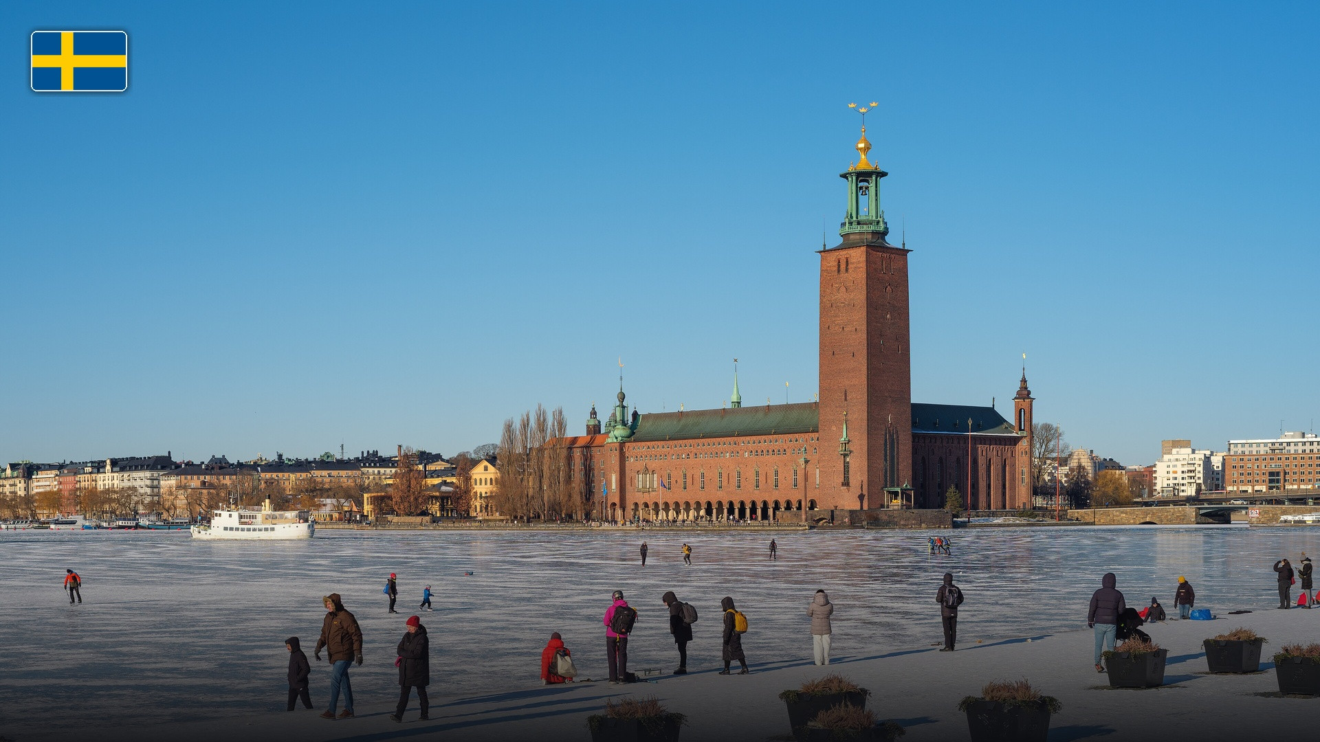 Stockholm City Hall standing proudly on the waterfront with its Three Crowns tower, with the flag of Sweden.