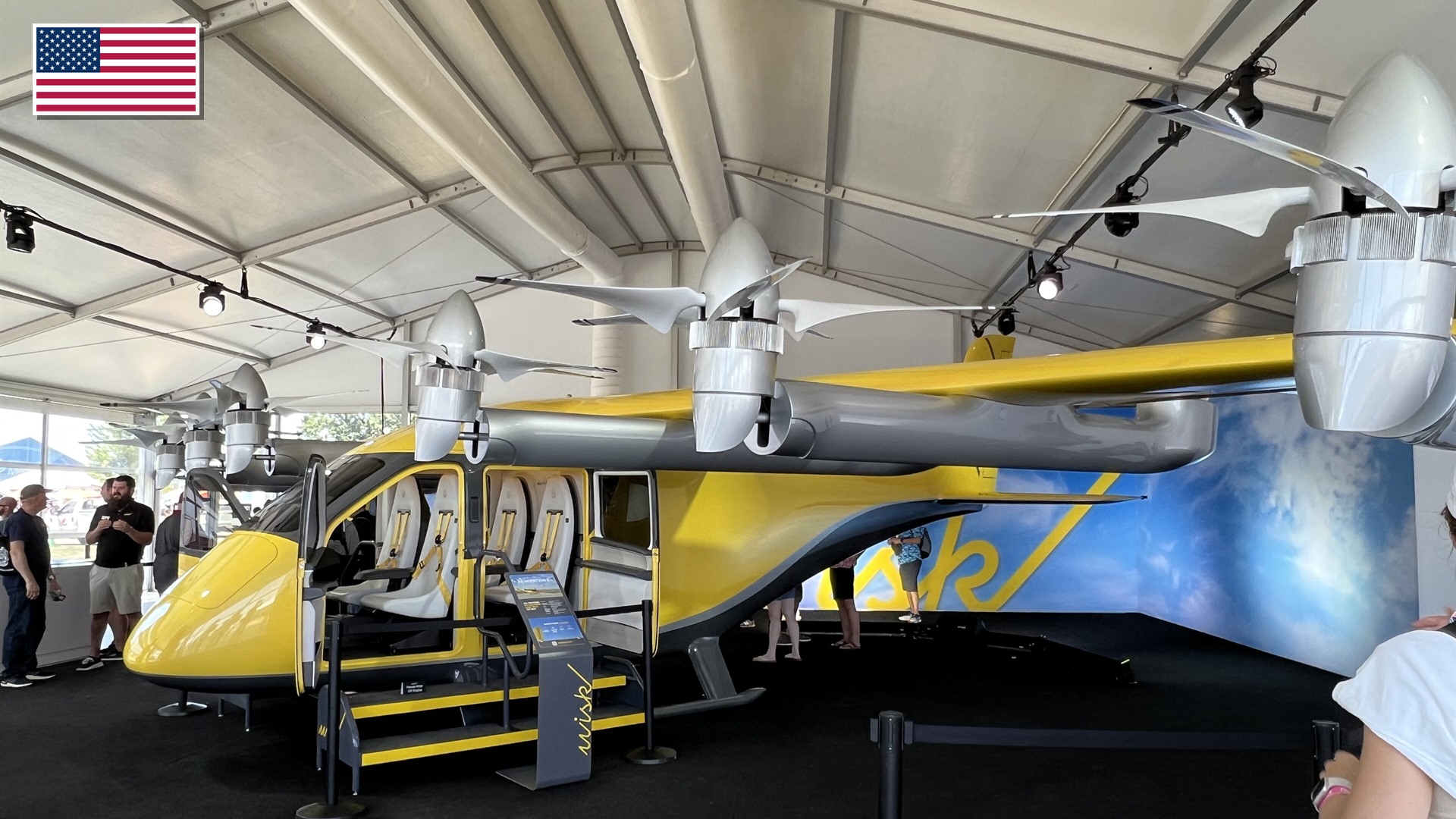 Yellow Wisk Aero Generation 6 autonomous 4-passenger air taxi with the US flag in the top-left corner.