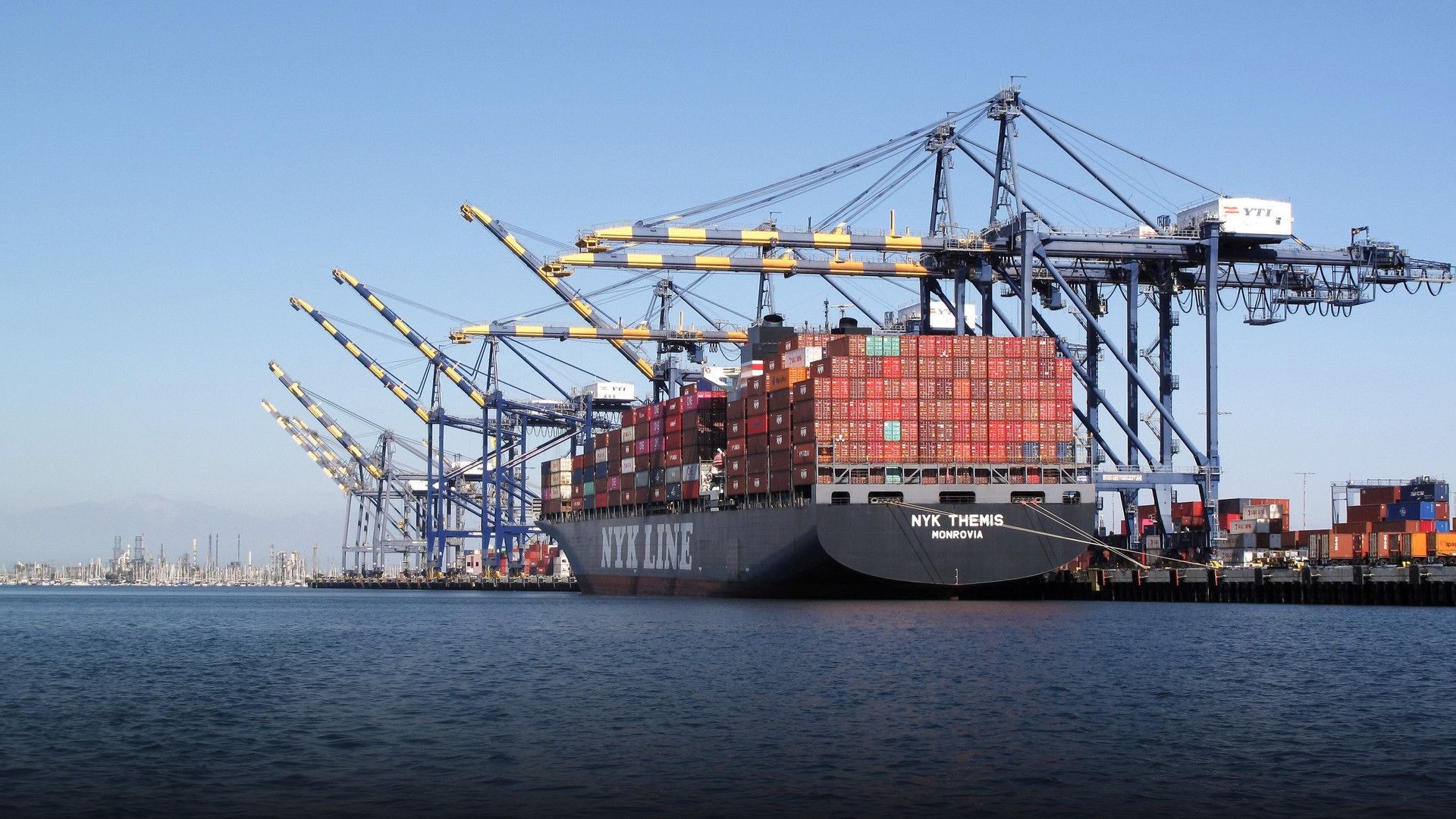 Enormous container ship laden with thousands of colorful cargo containers docked at the Port of Los Angeles terminal.