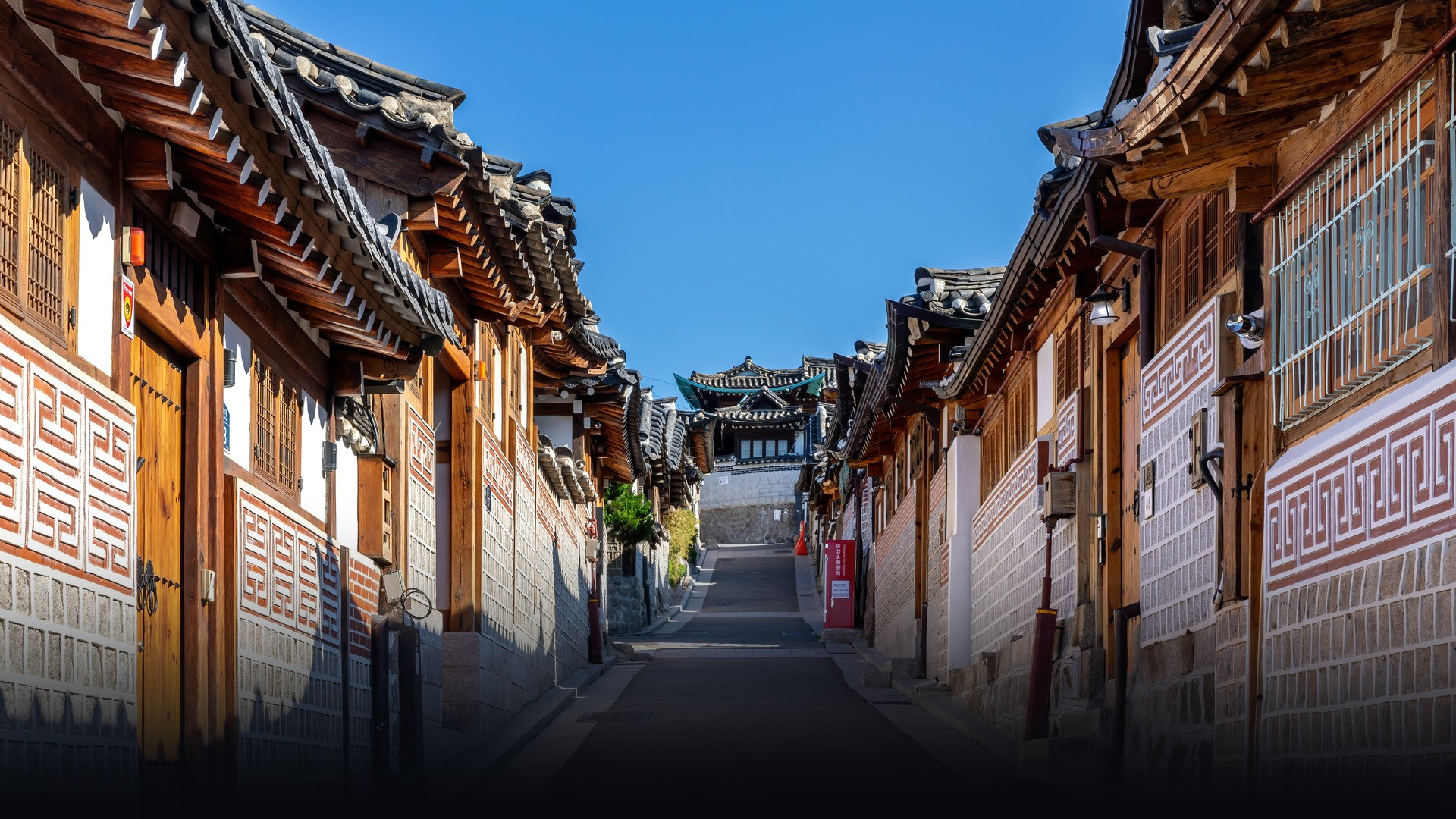 Traditional tiled roofs and stone alleys of Bukchon Hanok Village in Seoul under clear skies.