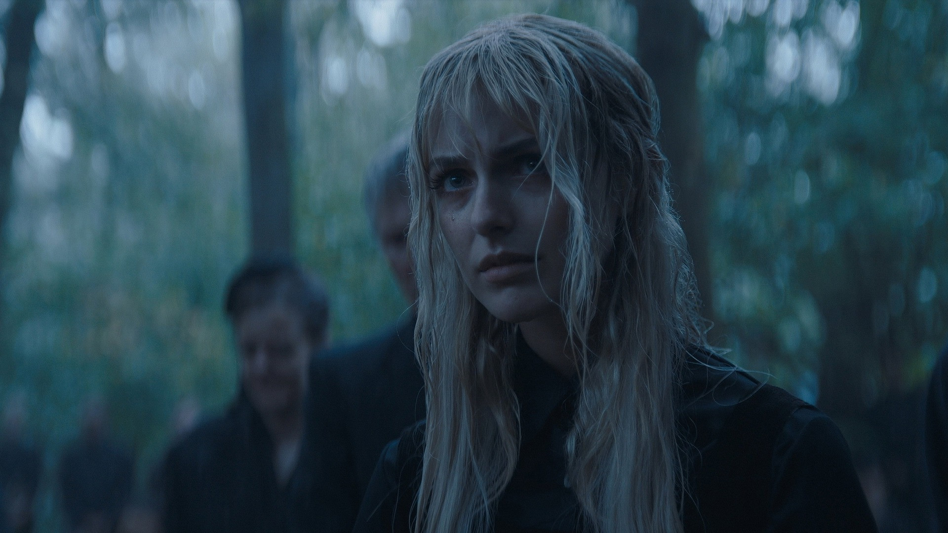 A young District 12 tribute with damp blonde hair looking anxious in the dark forested arena.
