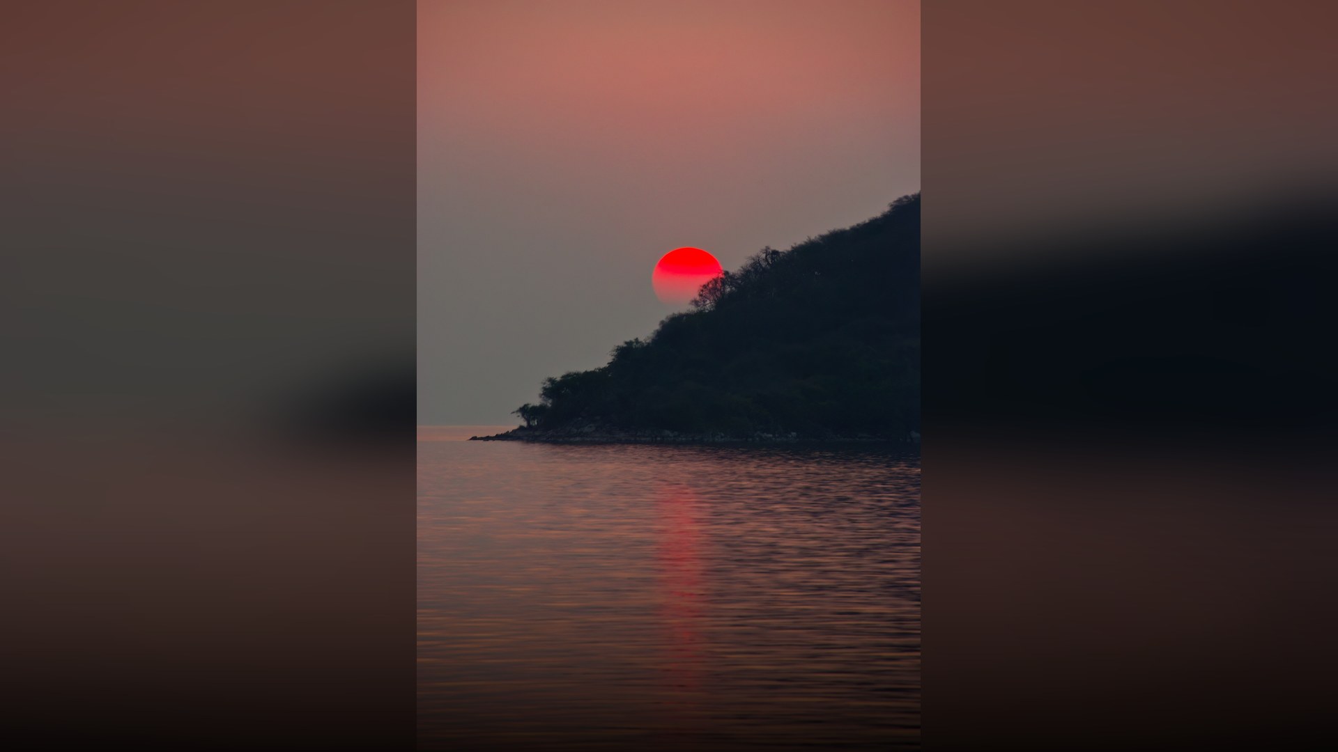 Golden sunset reflecting on the calm rippling waters of Lake Malawi with distant hills on the horizon.