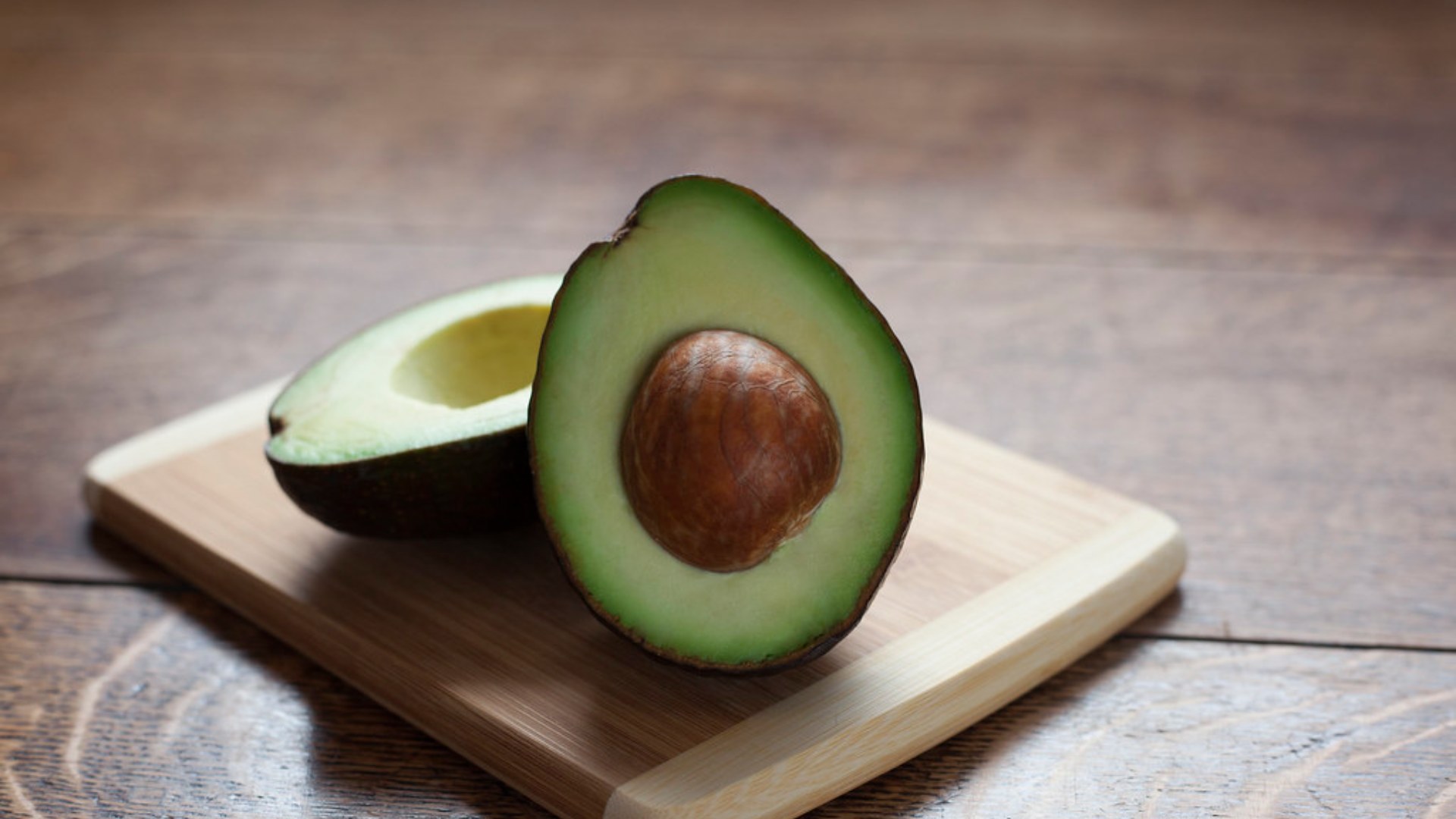 Halved avocado on a wooden chopping board