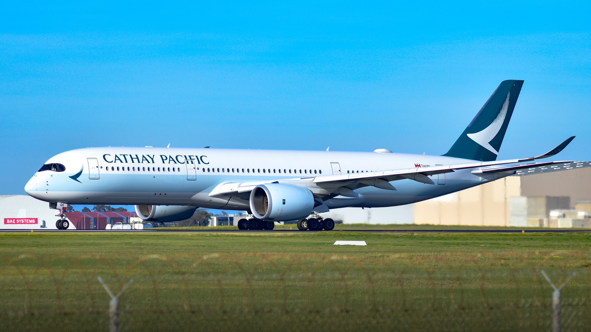 A Cathay Pacific Airbus A350-941 aircraft featuring its signature jade brushwing livery climbing over Melbourne.