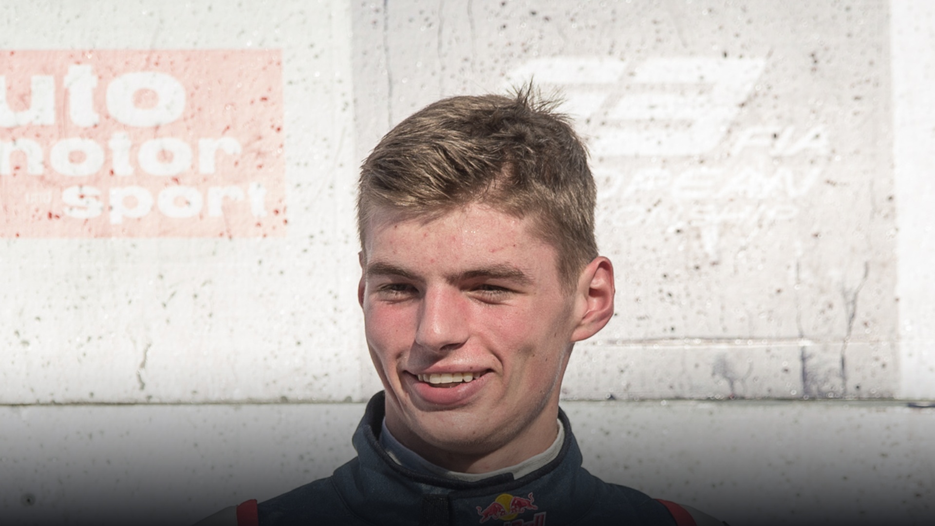 A teenage Max Verstappen smiling in his racing fire suit during his Formula 3 junior career.