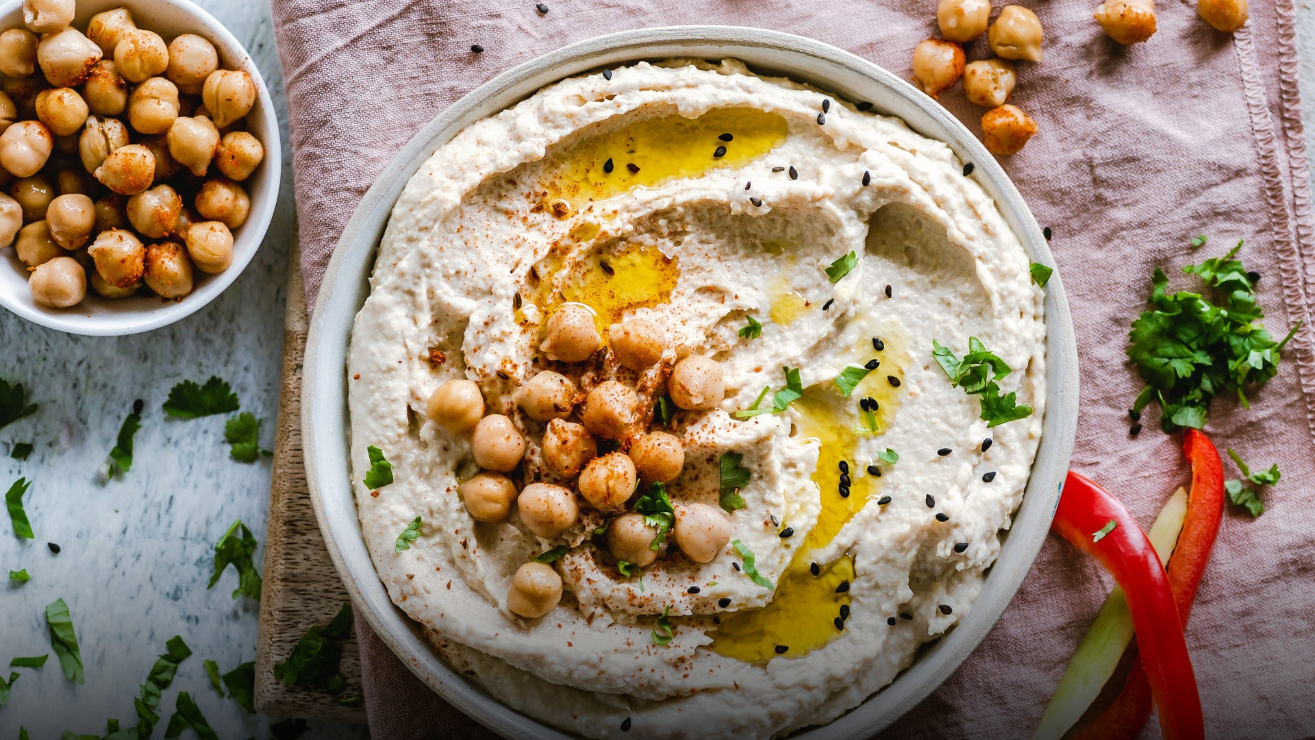 A vibrant bowl of smooth creamy hummus garnished with olive oil, paprika, whole chickpeas, and fresh parsley.