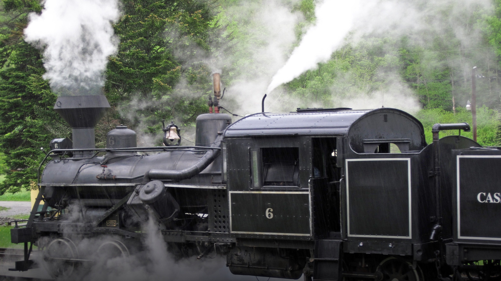 Historic black steam locomotive billowing thick white steam along mountain tracks in West Virginia