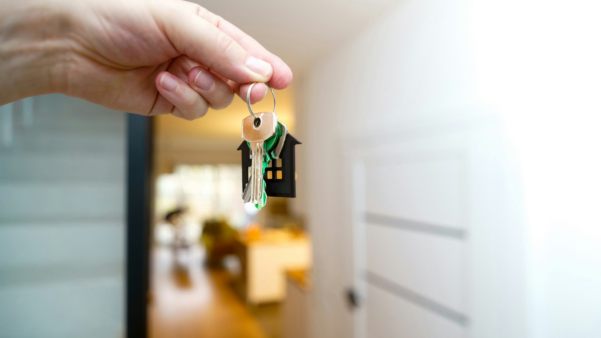 Hand holding house keys in front of a modern residential home entrance
