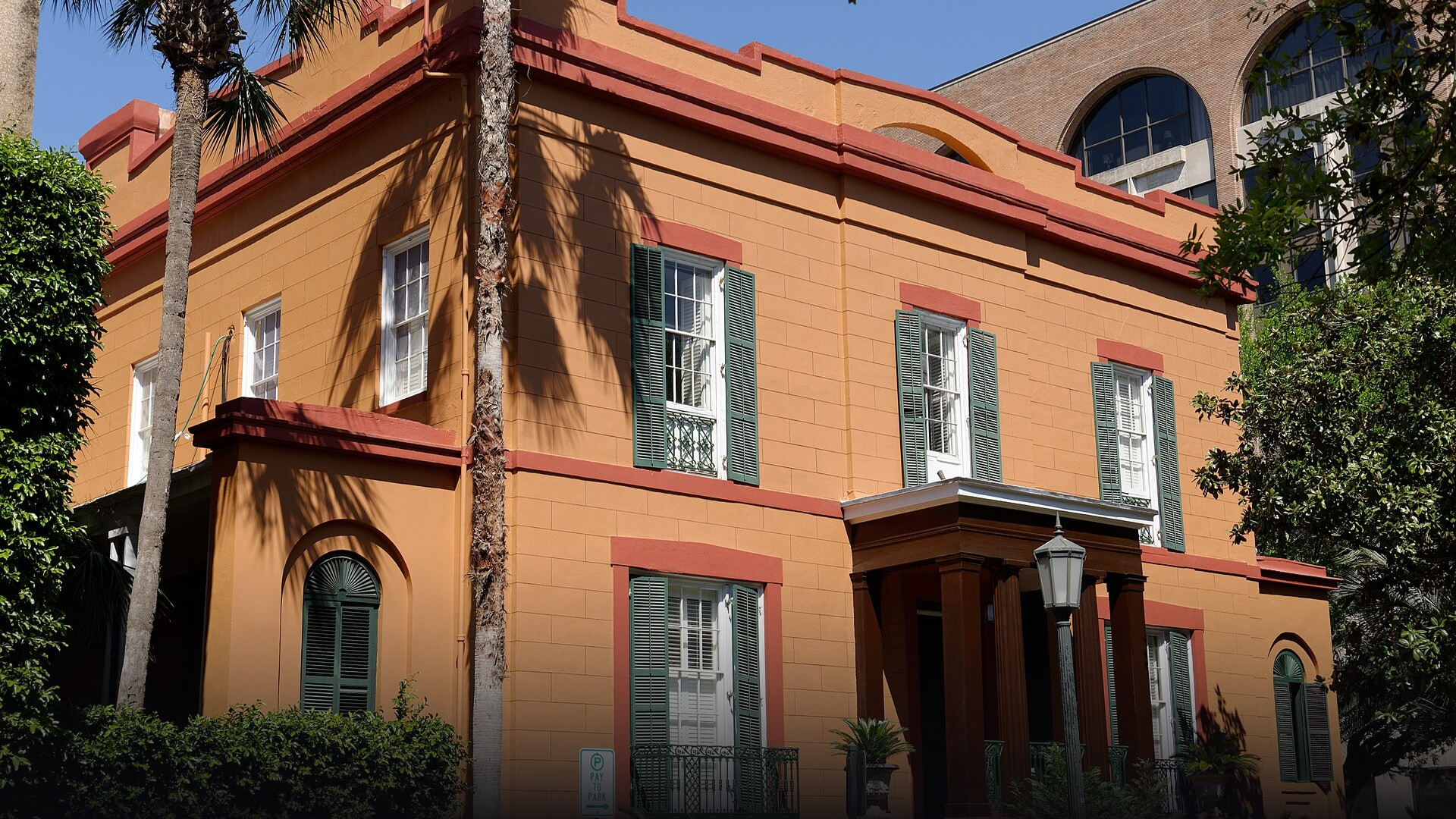 Imposing orange-hued Greek Revival facade and curved wrought iron balcony of the Sorrel-Weed House on Madison Square in Savannah.