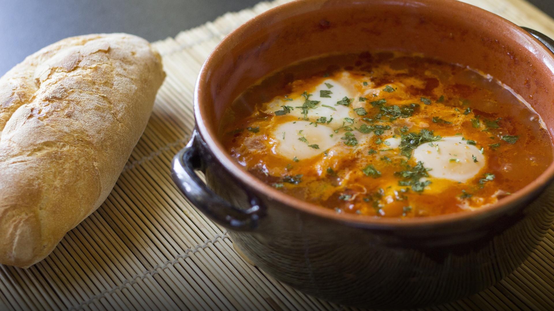 A sizzling cast iron skillet filled with rich red spiced tomato sauce and gently poached eggs garnished with fresh herbs.