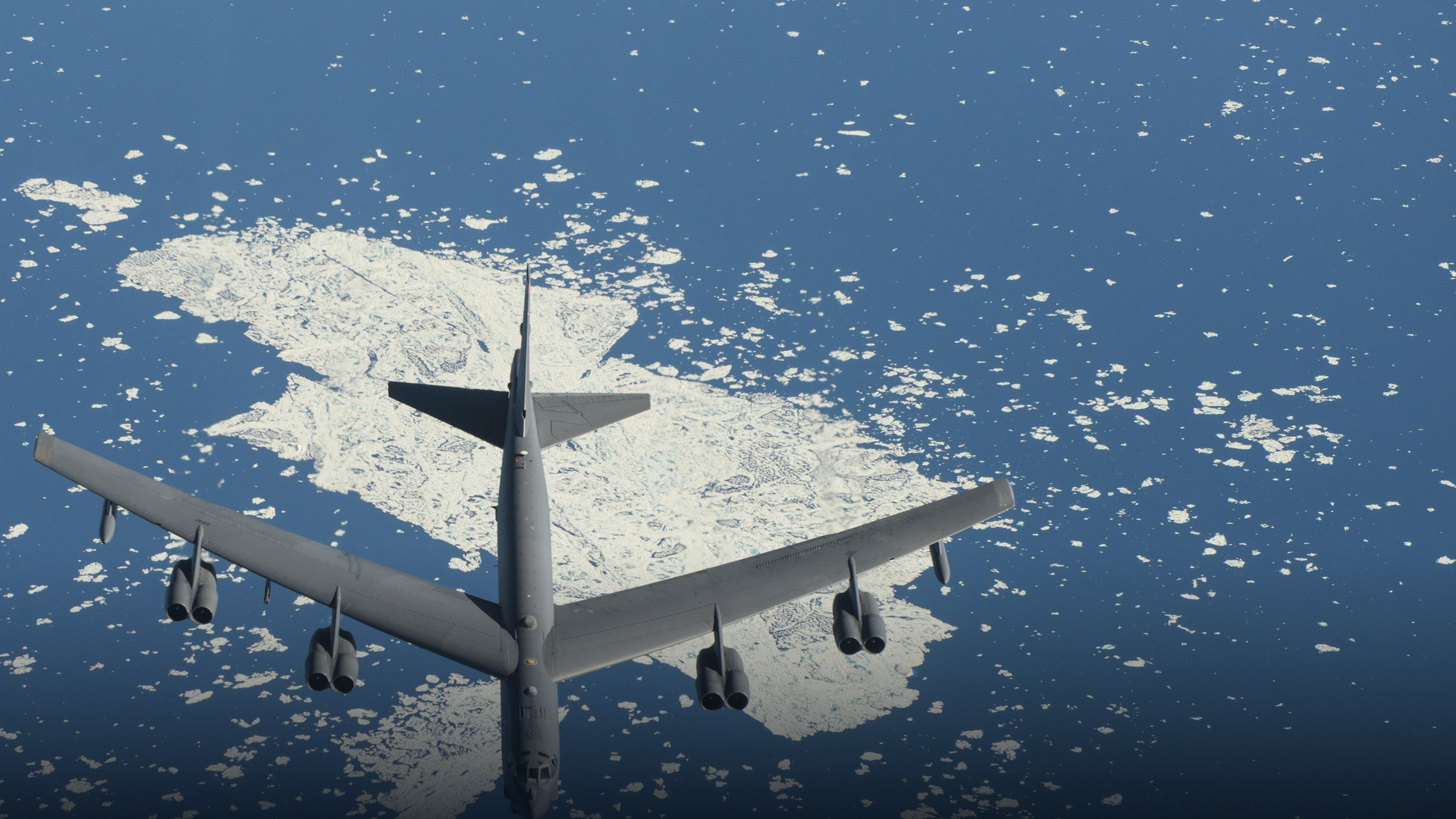 Eight-engine Boeing B-52H Stratofortress heavy bomber soaring over Arctic sea ice and cobalt blue ocean.