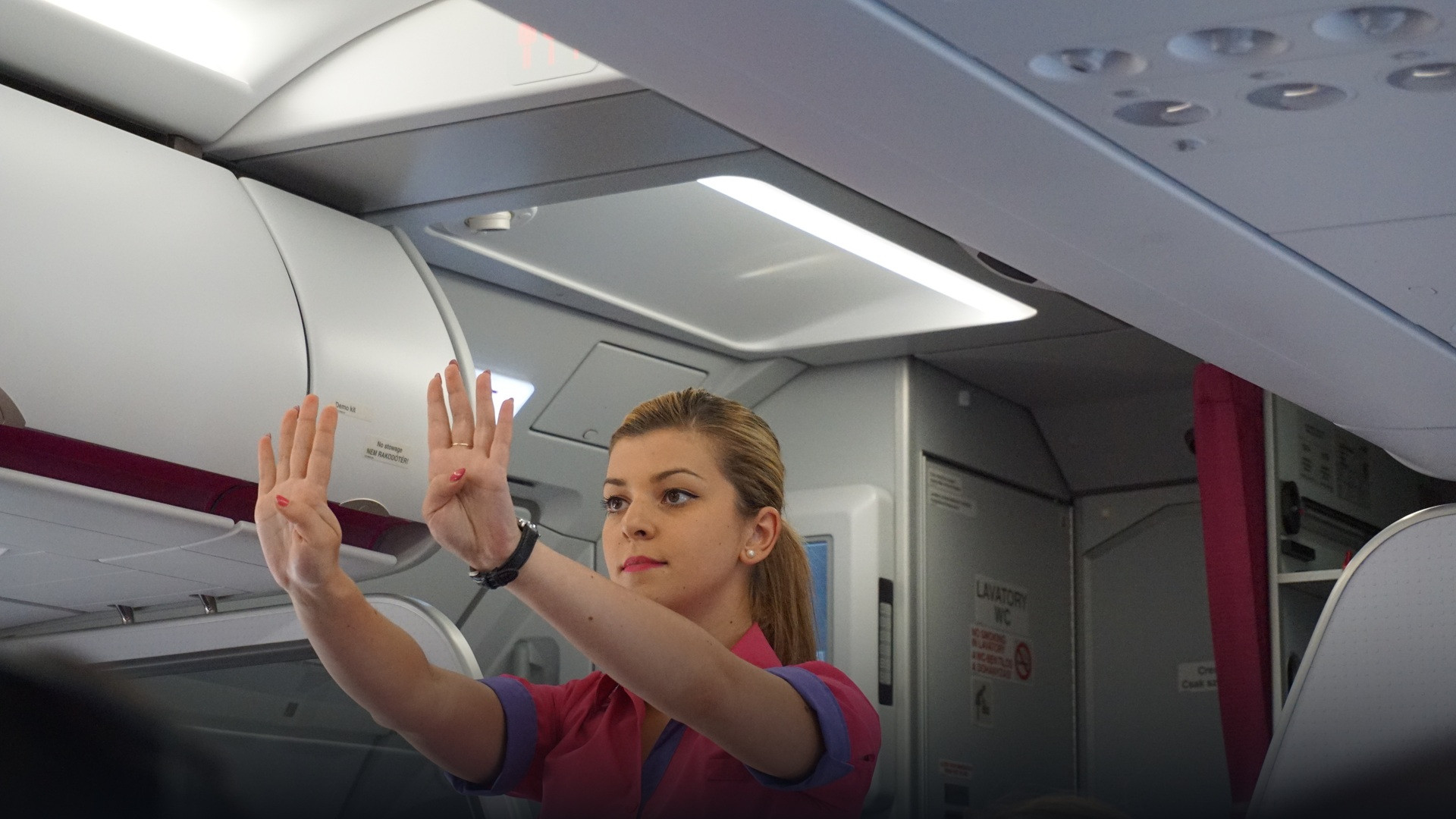 Flight attendant performing pre-flight safety demonstration inside commercial aircraft.