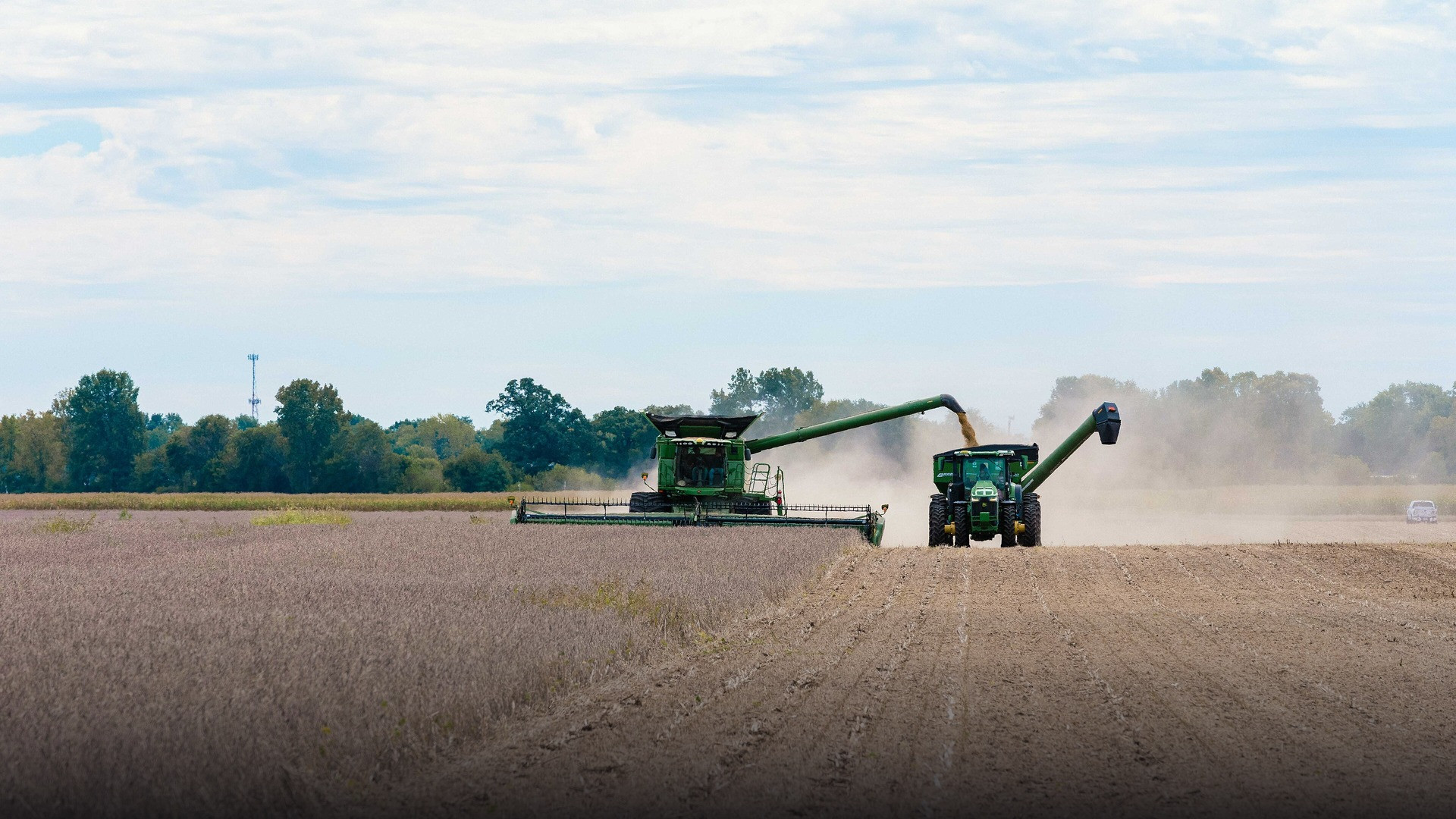 Large agricultural combine harvester gathering soybeans across expansive rural farmland in the American Midwest.