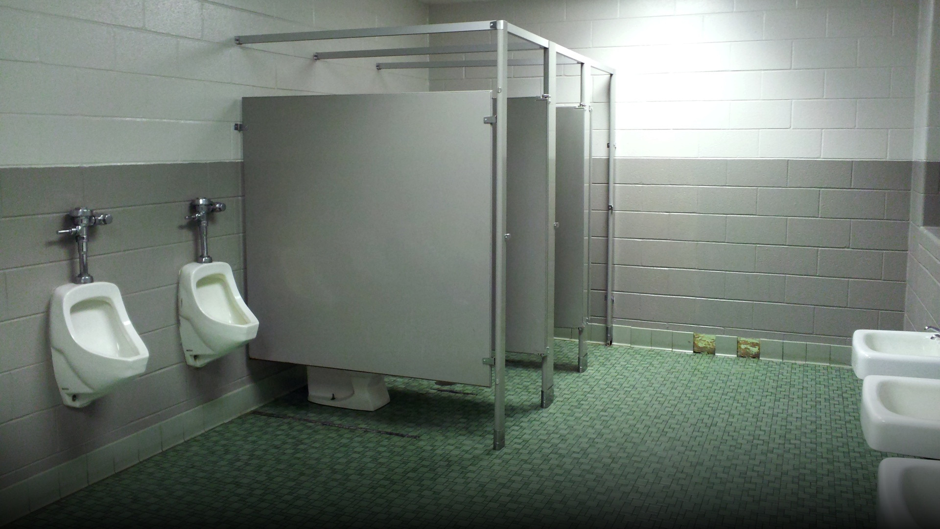 An American public restroom with suspended metal stall doors showing significant space at the bottom.