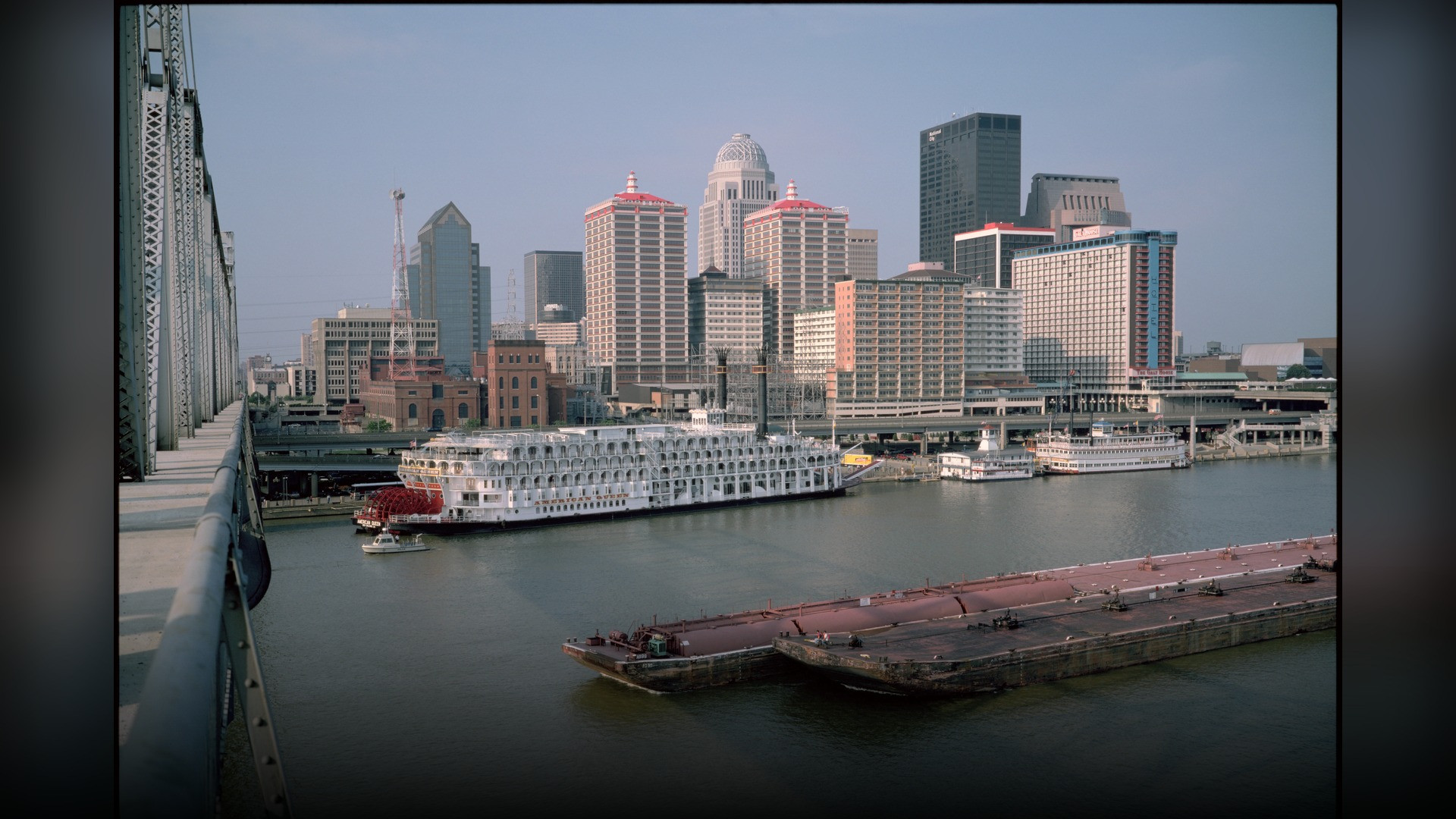 Louisville Kentucky downtown skyline reflected across the Ohio River under blue skies.
