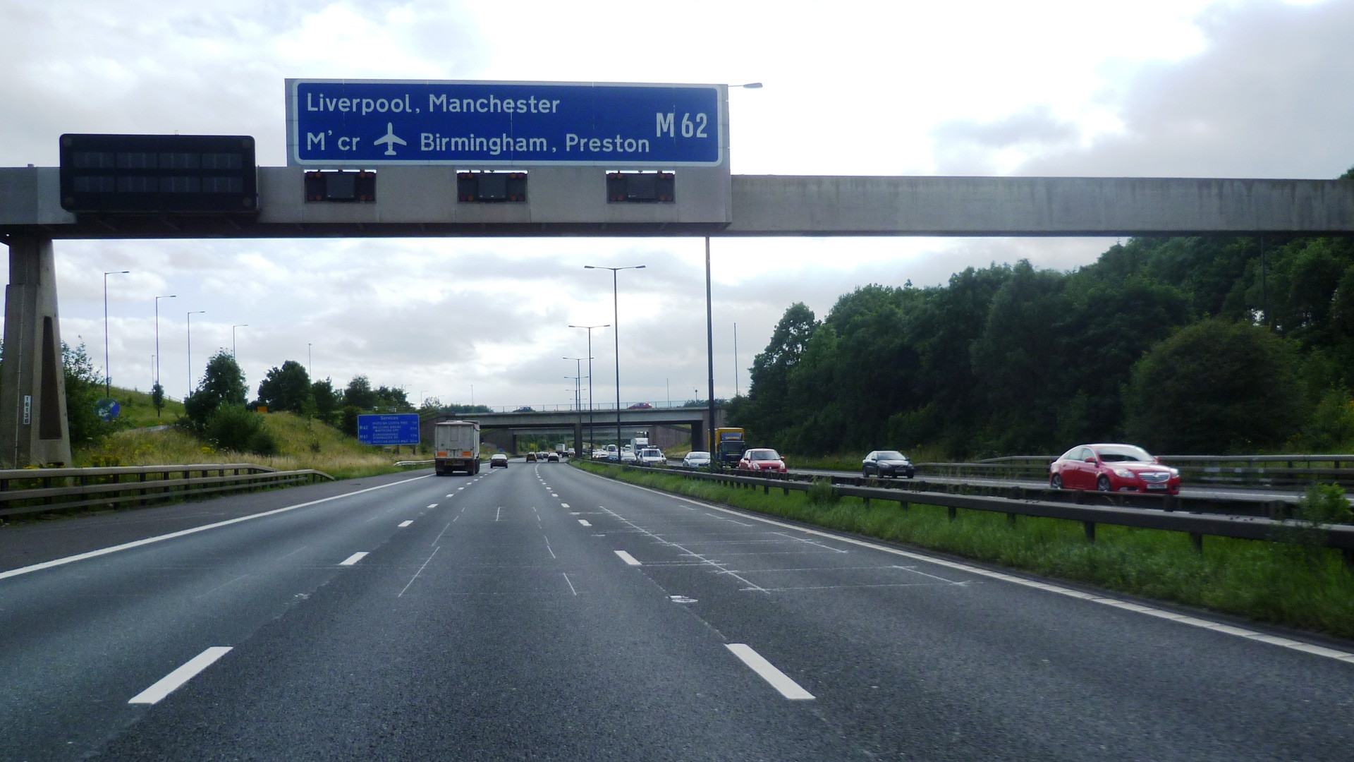 Wide perspective of a British motorway gantry spanning across flowing traffic under sunset skies.