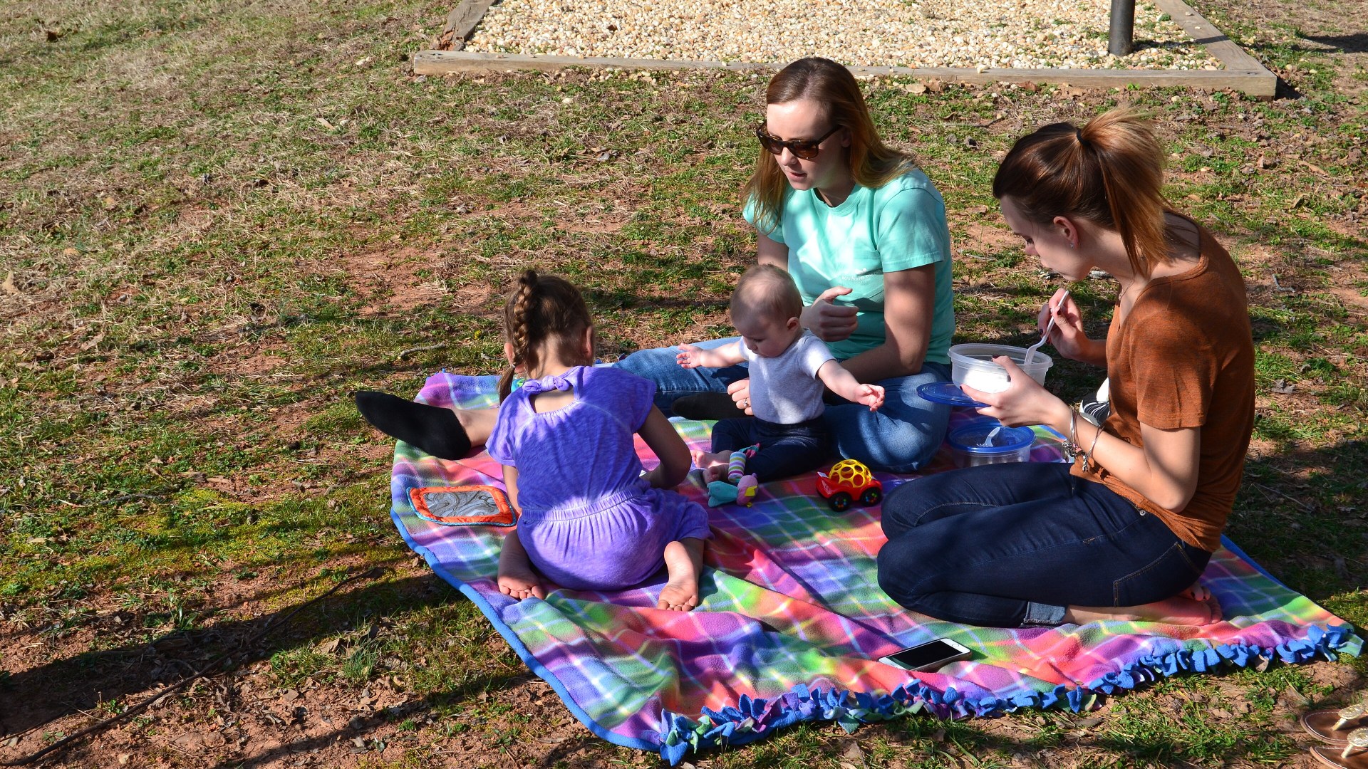A family enjoying an outdoor picnic together on a blanket in a state park.
