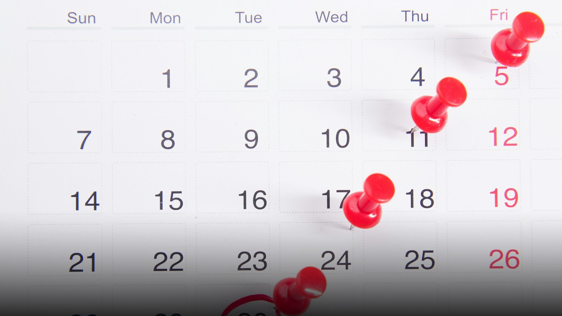 A printed monthly calendar grid with red pushpins marking days, showing Sunday as the first day of the week.