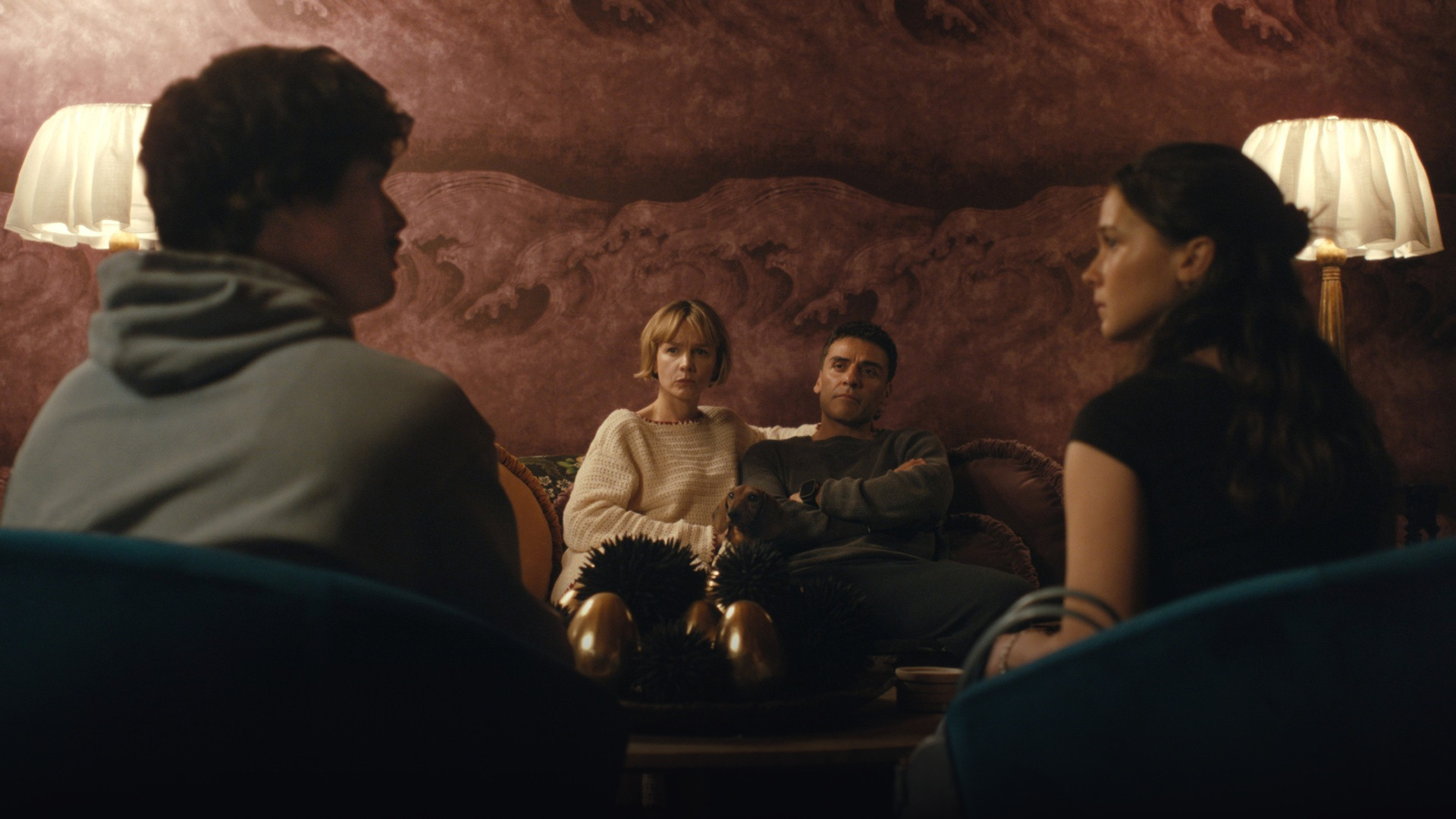 Oscar Isaac and Carey Mulligan seated on a sofa engaged in tense confrontation with Cailee Spaeny and Charles Melton.