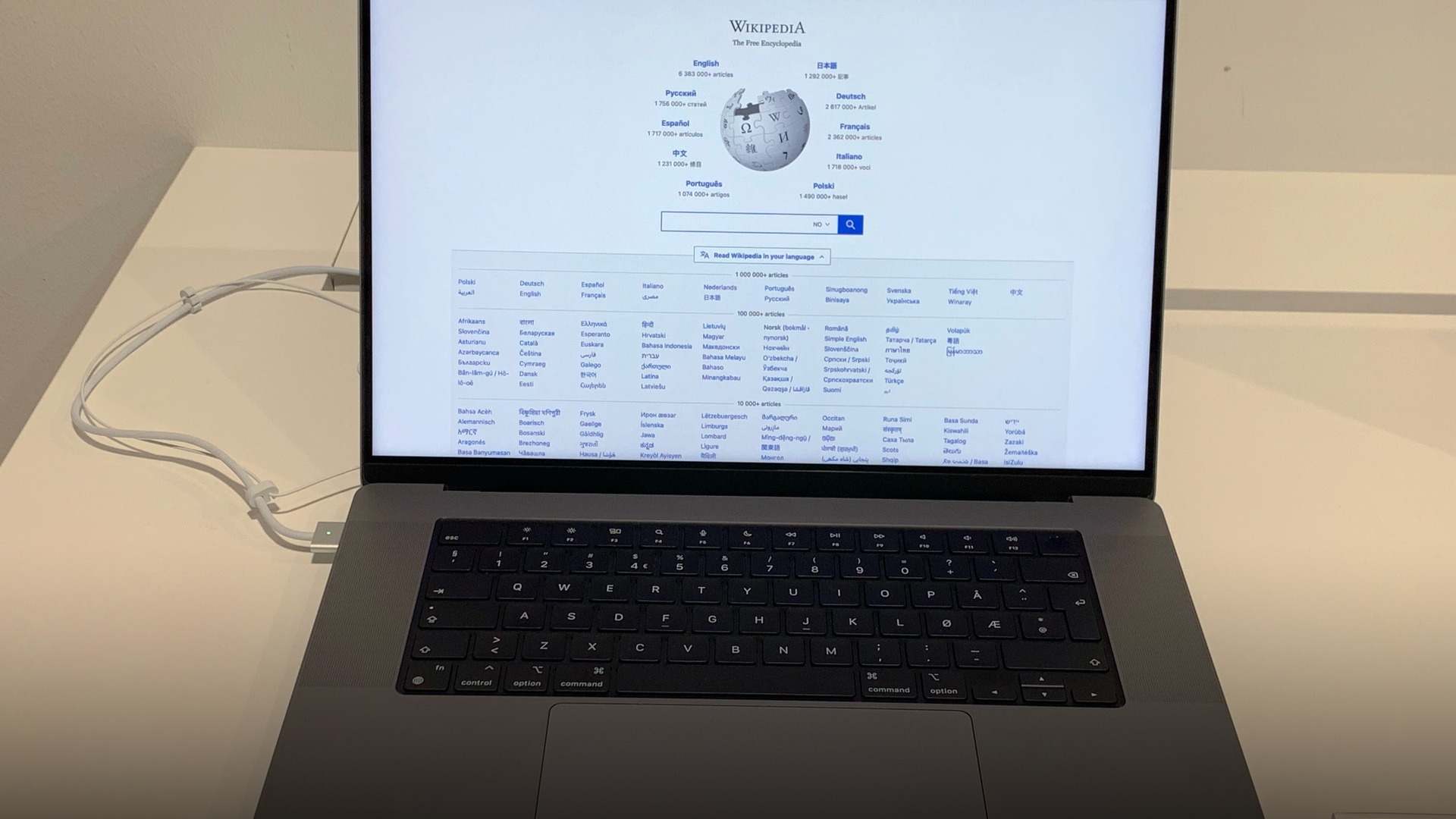Space gray 16-inch Apple MacBook Pro laptop open on a wooden desk showing its keyboard and Liquid Retina XDR display.