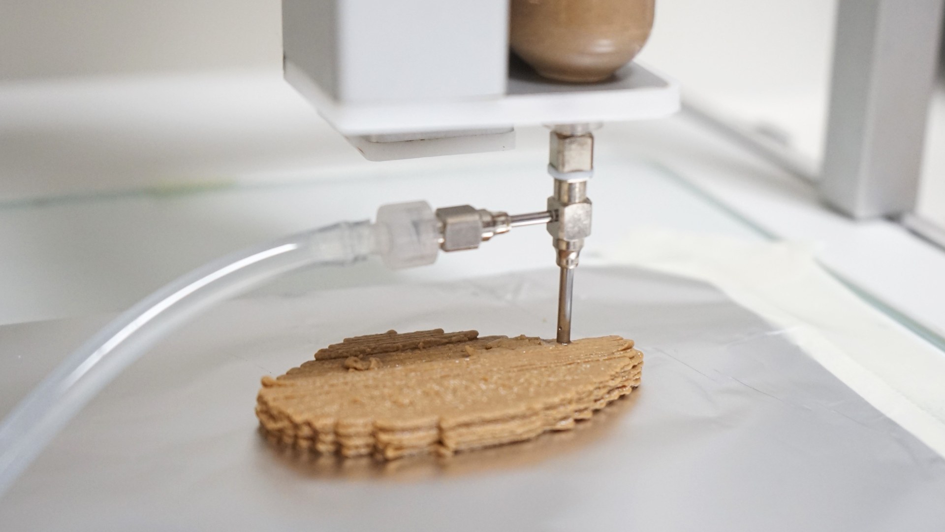 Close-up of a 3D food printer nozzle extruding nutrient paste layers onto a platform