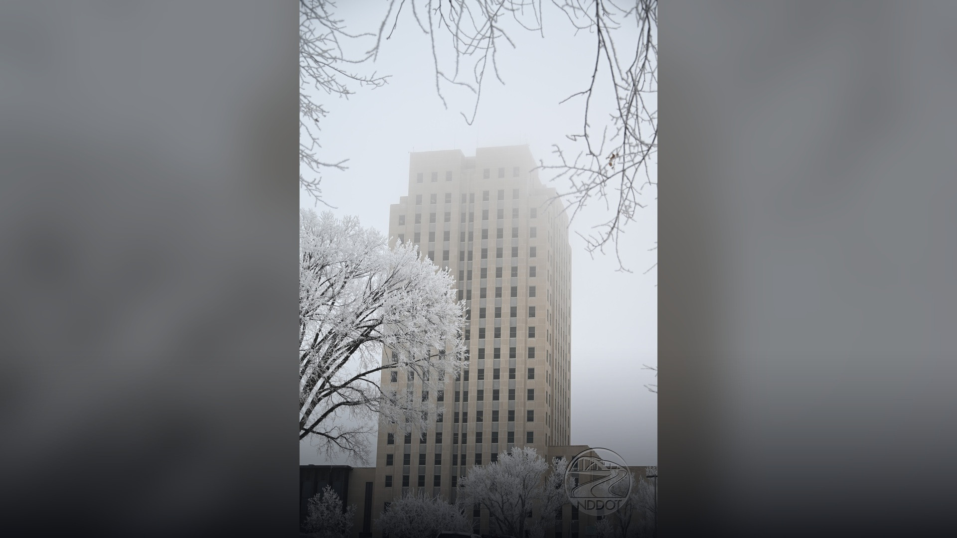 The tall Art Deco North Dakota State Capitol tower surrounded by hoarfrost and snowy grounds.